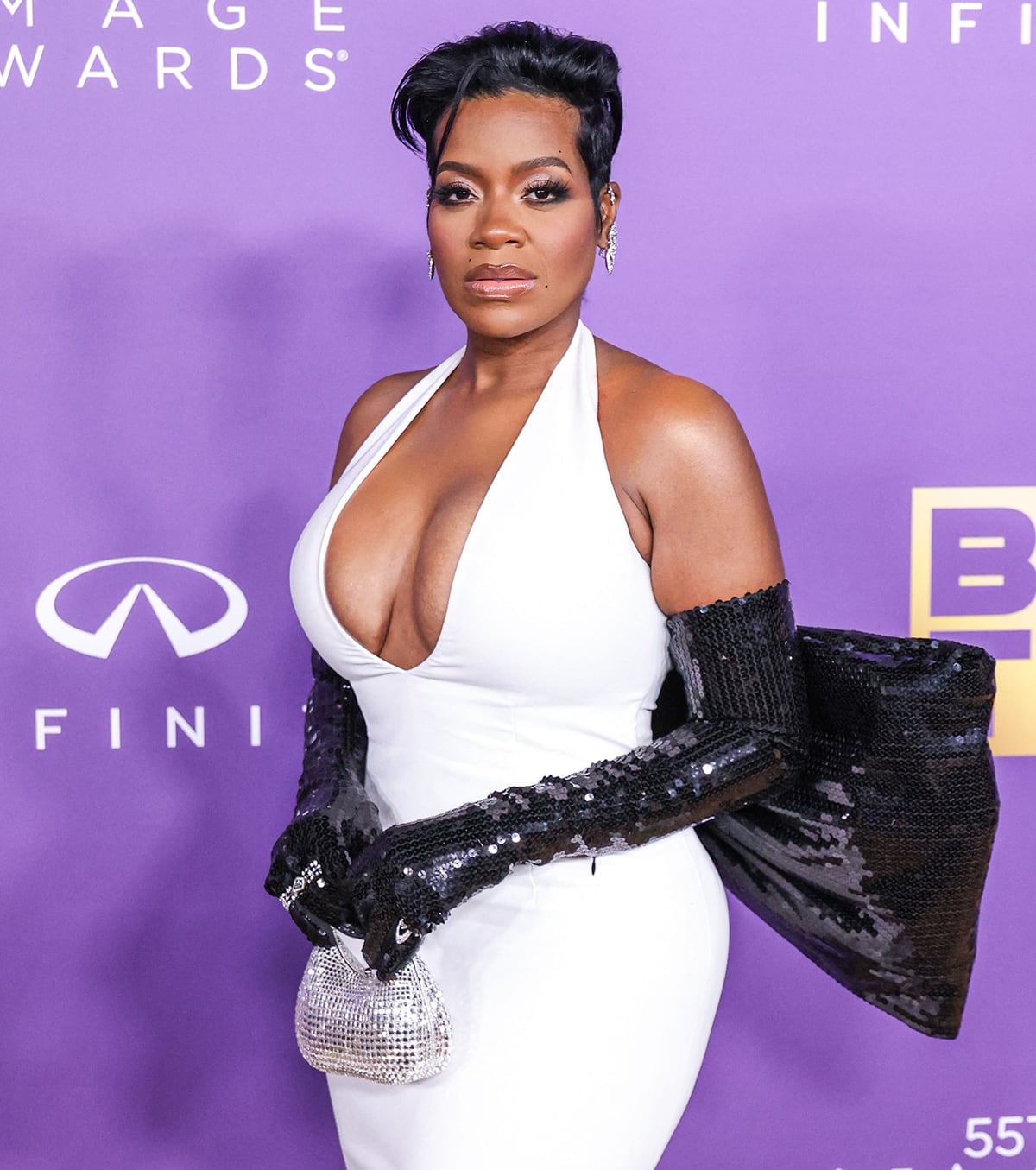 Wearing her short hair up and accentuating her features with soft, smokey eyeshadow and lip gloss, Fantasia Barrino styles her retro look with Messika diamond jewelry and a Judith Leiber silver clutch
