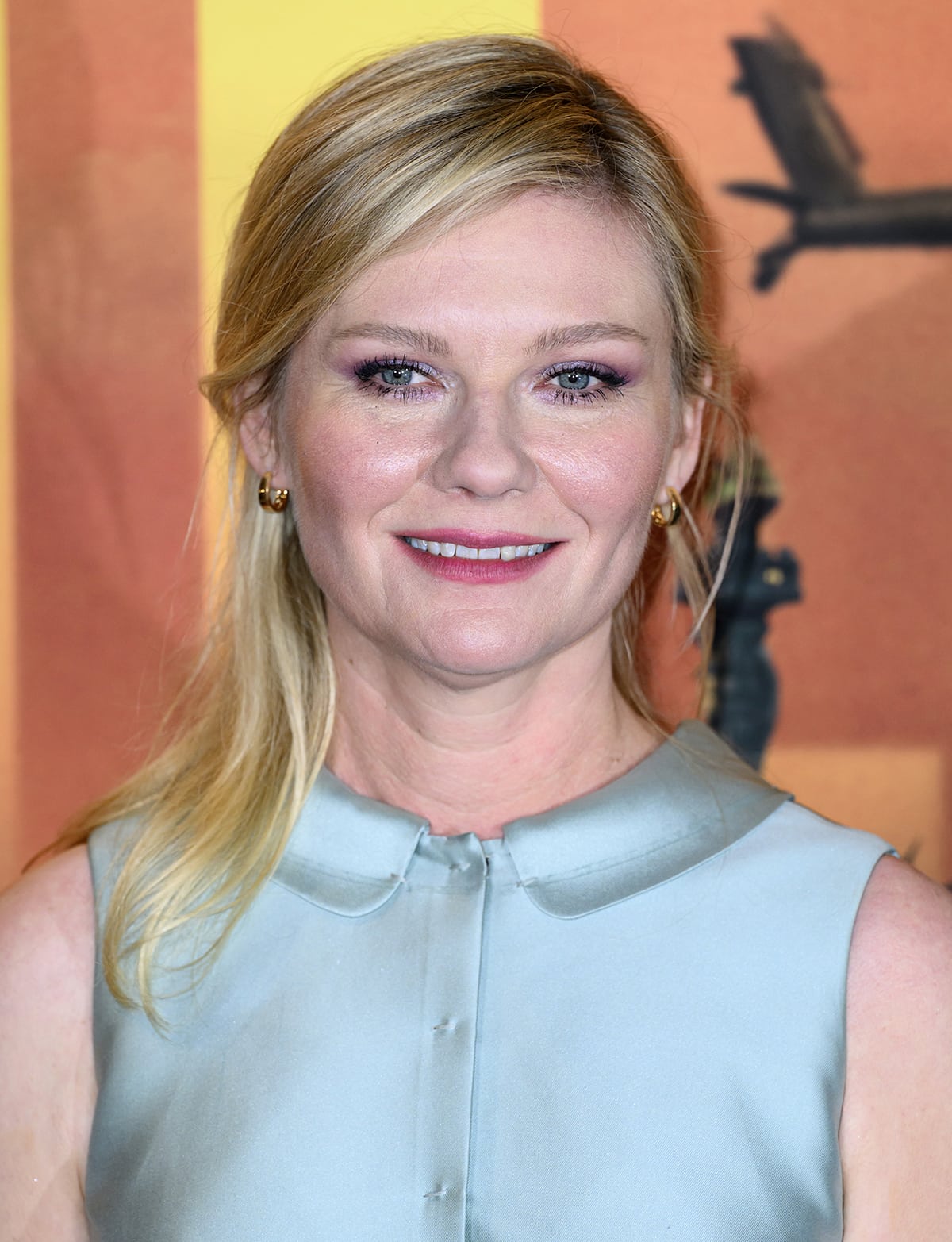 Kirsten Dunst styles her blonde hair in a half updo and wears soft pink makeup with subtle eyeshadow and pink lipstick