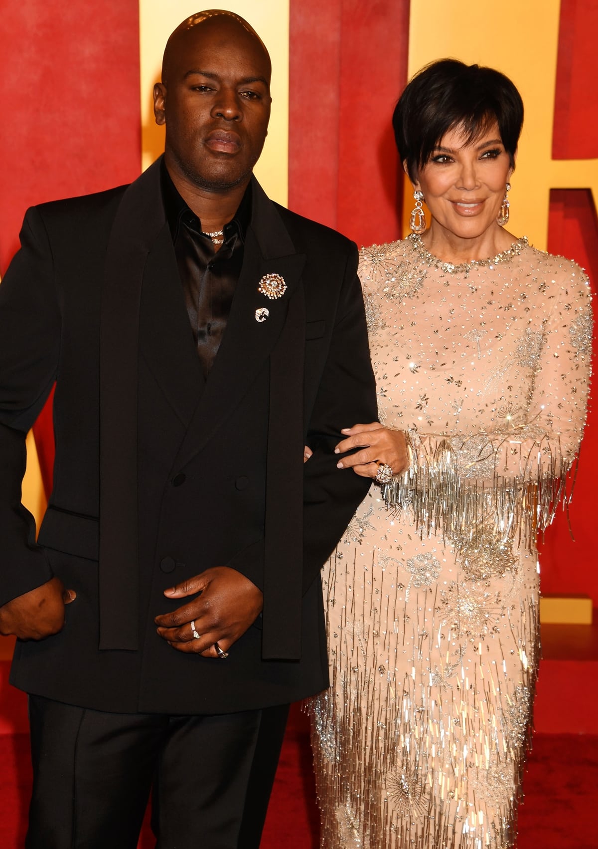 Kris Jenner and Corey Gamble walking hand in hand on the Vanity Fair Oscar Party red carpet, Kris dazzling in a crystal-embroidered Oscar de la Renta gown and Corey in a classic black tuxedo