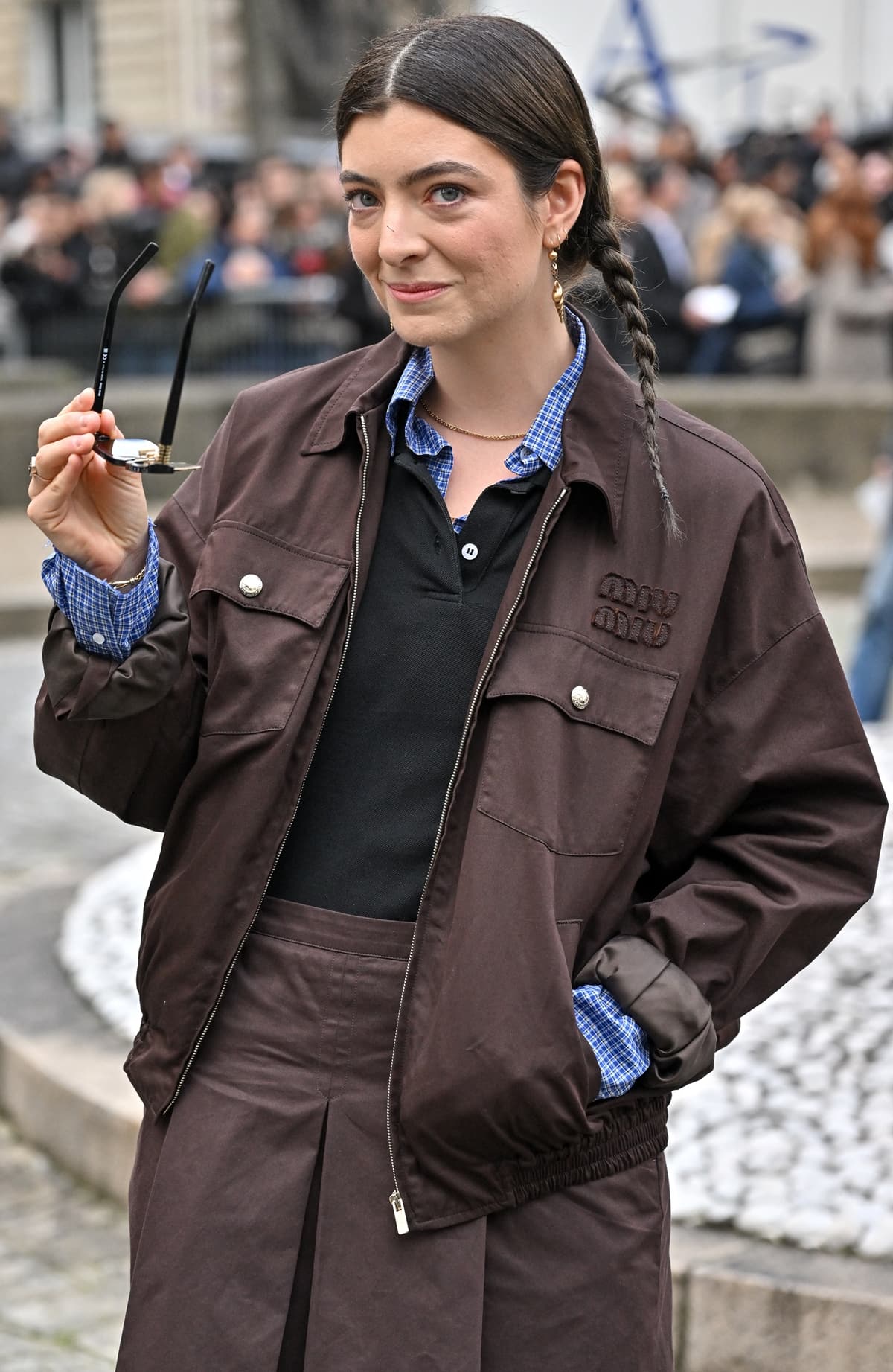 Lorde, in a masterfully layered Miu Miu look, pairs a black wool knit polo with a peek of blue checkered shirt, elevating geek chic at Paris Fashion Week, March 5, 2024