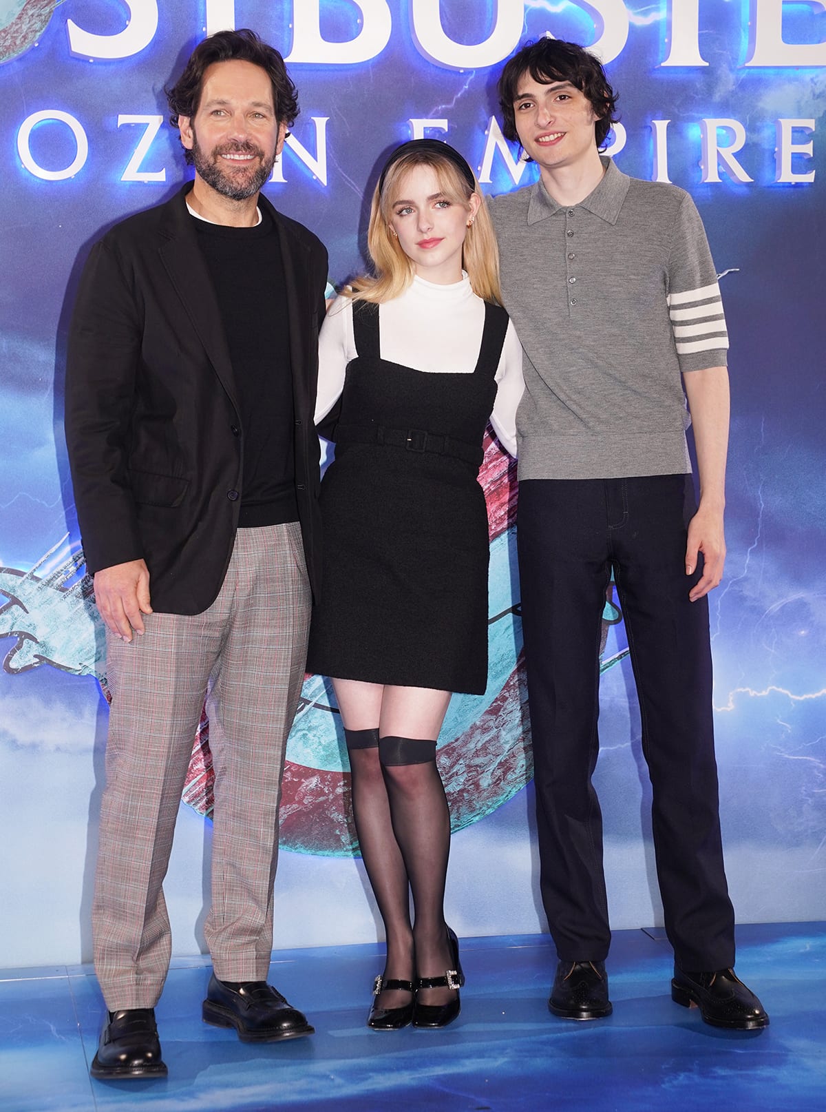 Mckenna Grace is bewitching in a black pinafore mini-dress with a white long-sleeved top, knee-length stockings, and Mary Janes pumps with Paul Rudd and Finn Wolfhard at the London photocall for Ghostbusters: Frozen Empire on March 21, 2024