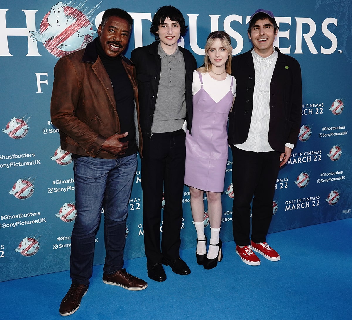 Mckenna Grace stands out in a lilac pinafore dress with a white tee, ruffled socks, and Mary Jane pumps as she poses with co-stars Ernie Hudson and Finn Wolfhard and director Gil Kenan at the UK gala screening of Ghostbusters: Frozen Empire at the Ham Yard Hotel on March 21, 2024