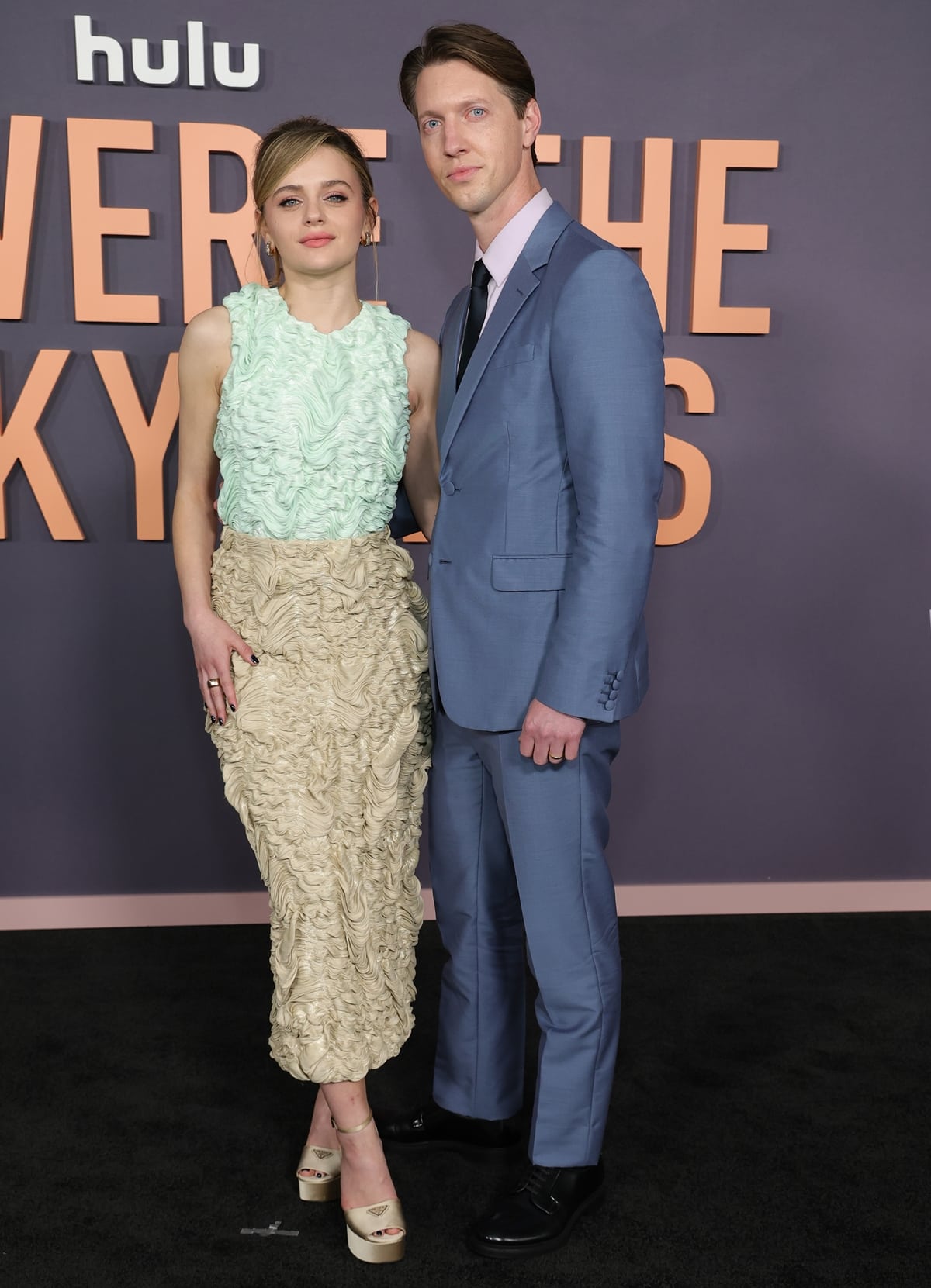 Newlyweds Joey King and Steven Piet make their red carpet debut as a married couple in coordinating chic attire, with Joey in a Prada gown and Steven in a sleek blue suit at the premiere of "We Were The Lucky Ones."
