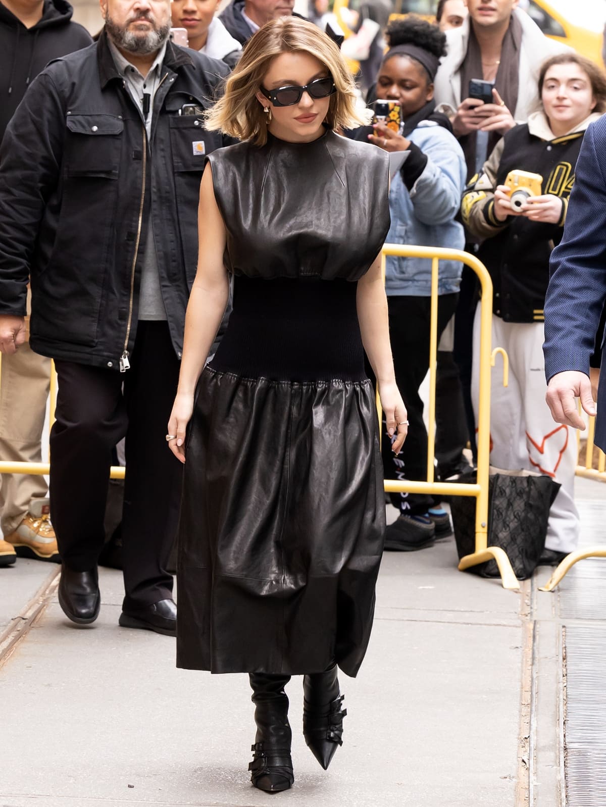 Sydney Sweeney exudes a captivating blend of biker chic and 1940s glamour in a $5,400 black leather 'The Uni' dress by Khaite, complete with a mock-neck top and keyhole slit detailing, as she steps out in Manhattan's Upper West Side to tape an episode for The View