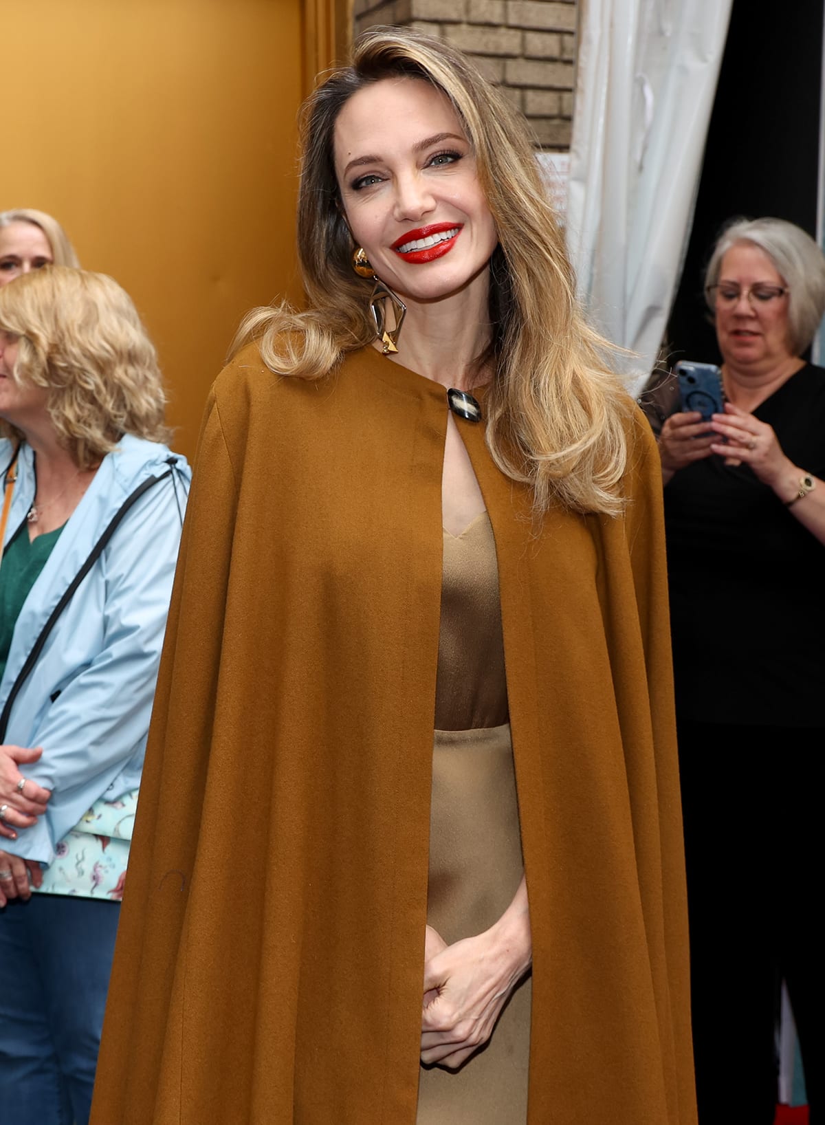 Angelina Jolie, wearing a gold dress and a burnt-orange cape, reveals how serious her 15-year-old daughter Vivienne is with her assistant role in the production of The Outsiders