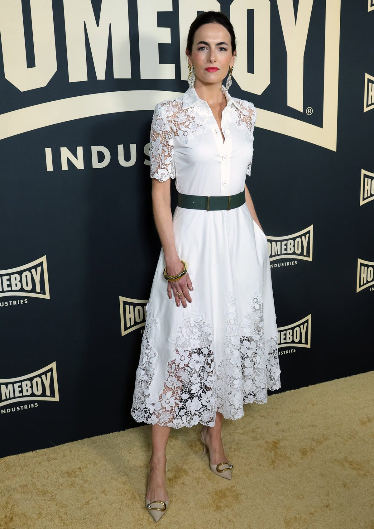 Camilla Belle stuns in a white lace Monique Lhuillier shirtdress paired with Alexandre Birman’s elegant nude slingback pumps, adding polish with Alexis Bittar jewelry