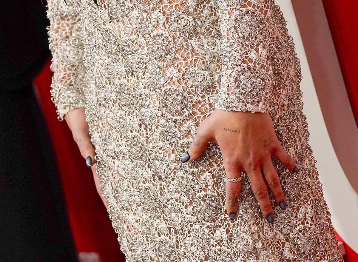 Dua Lipa's hand, tattooed with 'PATIENCE' and adorned with Tiffany & Co. rings, adds a touch of sparkle to her luxurious ensemble