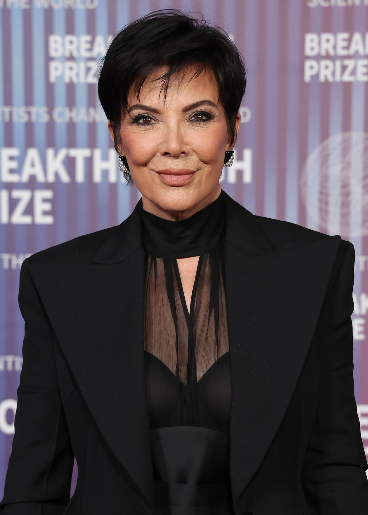 Kris Jenner wears her signature glam, including her pixie cut, smokey eyes, and nude lipstick