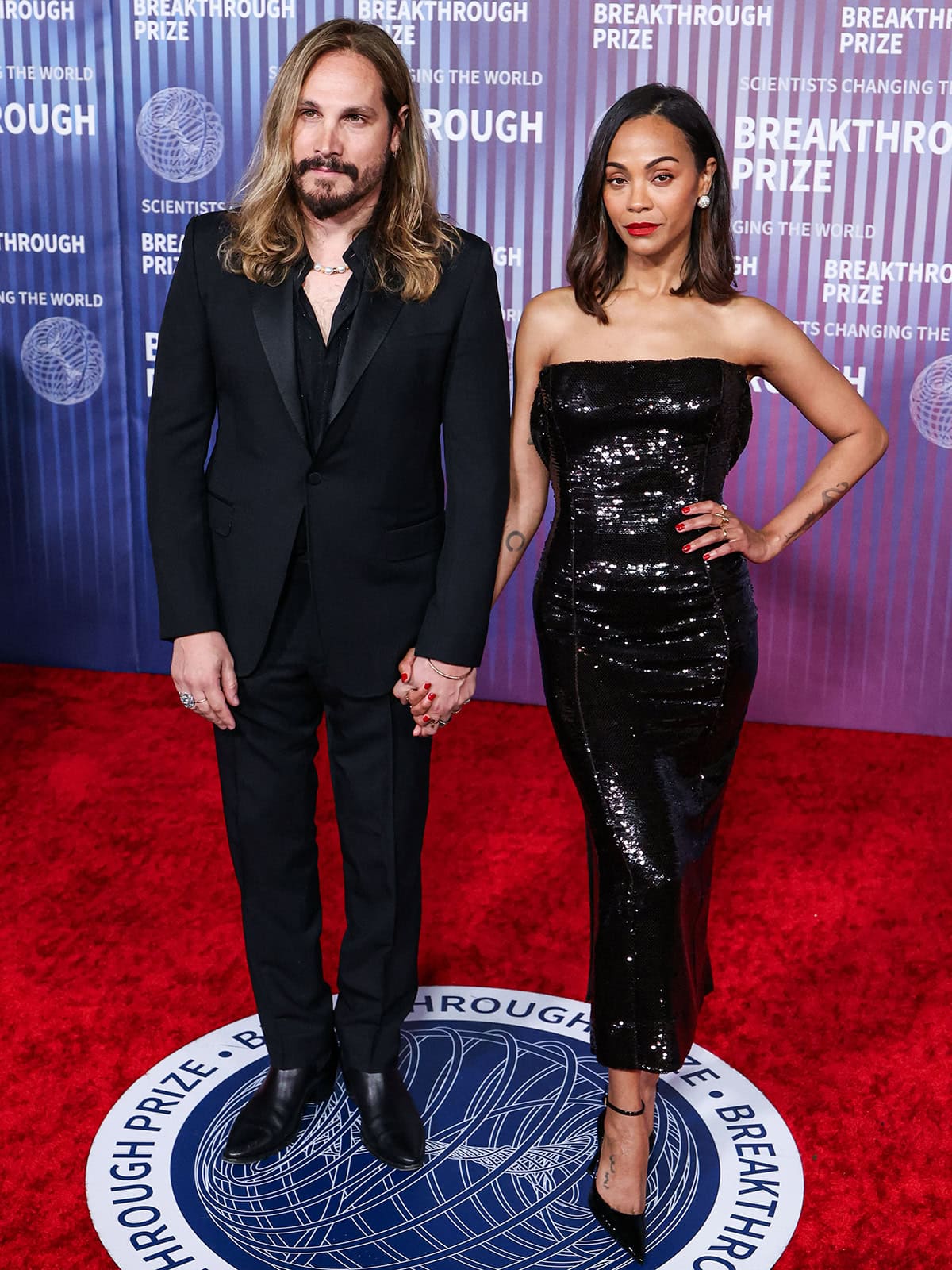 Marco Perego and Zoe Saldaña hold hands in black ensembles at the 10th Annual Breakthrough Prize Ceremony at the Academy Museum of Motion Pictures on April 13, 2024