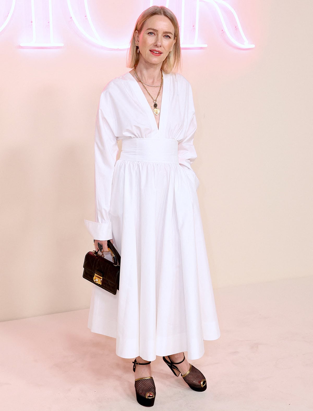 Naomi Watts is radiant in an elegant white Dior midi dress featuring a plunging neckline, a waistband, and long sleeves