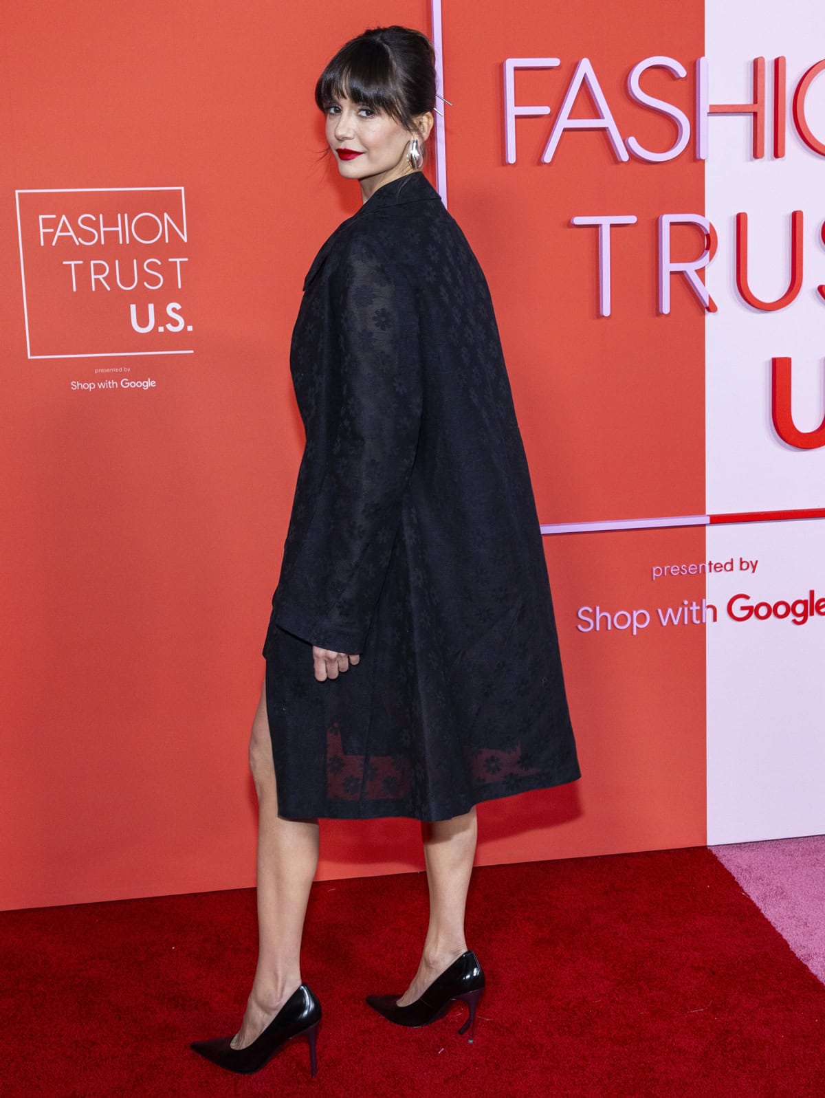 Nina Dobrev dazzles in an all-black Tory Burch ensemble, featuring a floral-adorned mini-dress and a semi-sheer matching coat, at the 2024 Fashion Trust US Awards in Los Angeles