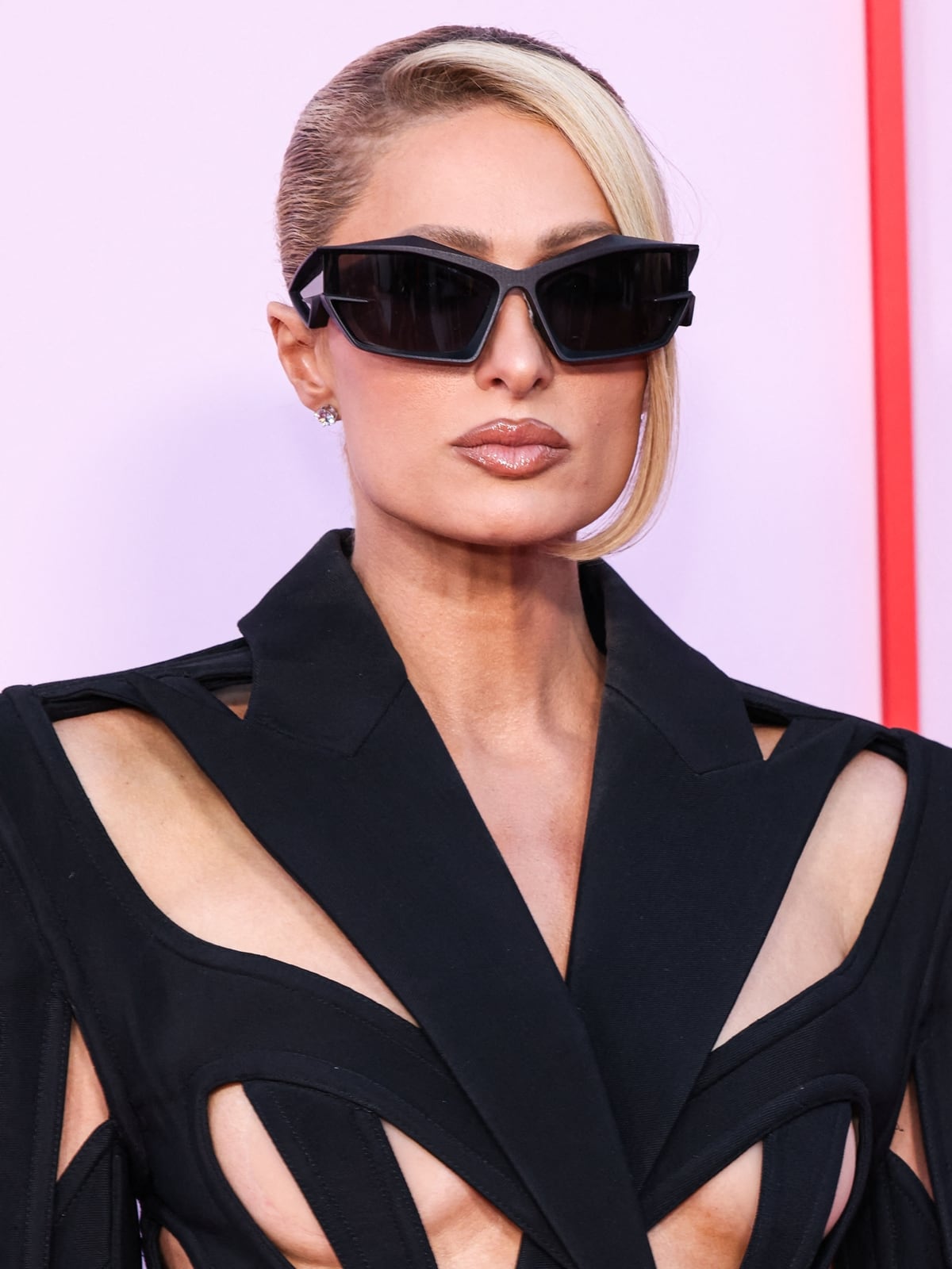 Paris Hilton's minimalistic approach to accessories allows her bold Mugler dress to remain the focal point, complemented by simple diamond studs and oversized square sunglasses