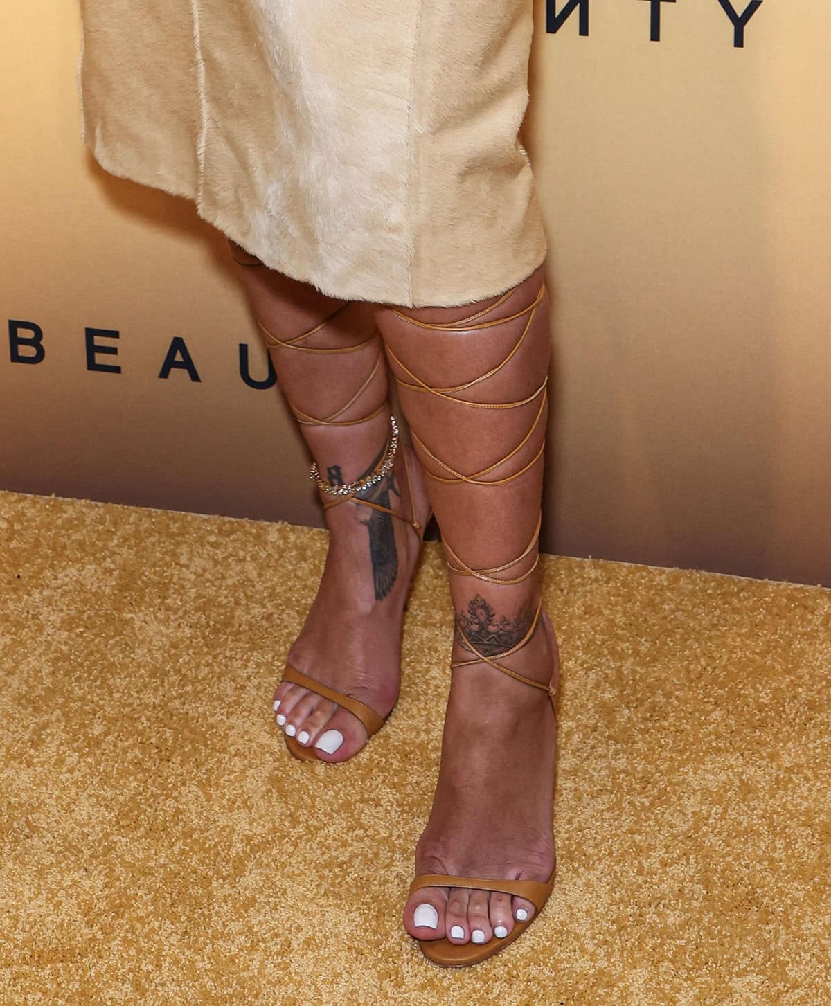 Rihanna slips her white-pedicured feet into a pair of tan gladiator sandals with thin wraparound lace-up straps and high heels