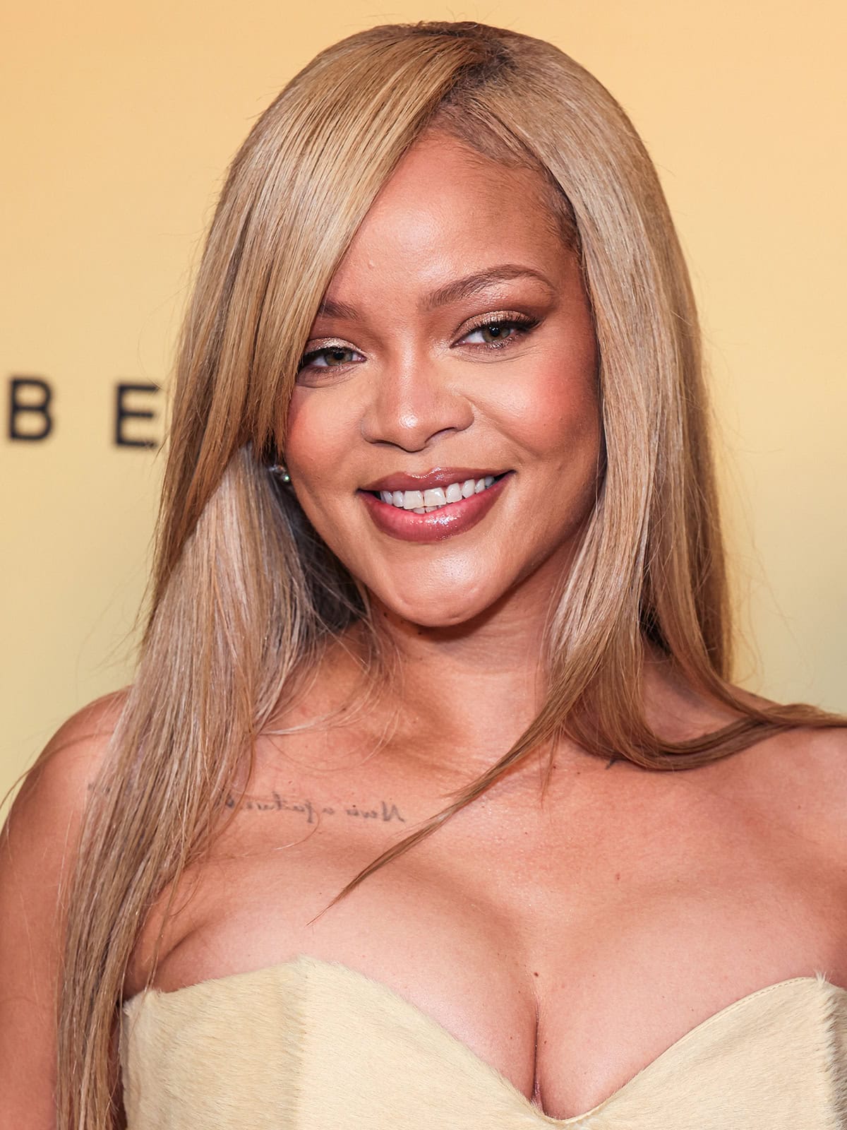 Rihanna uses Fenty Beauty makeup to achieve a golden hour glow and styles her blonde hair straight with a deep side part