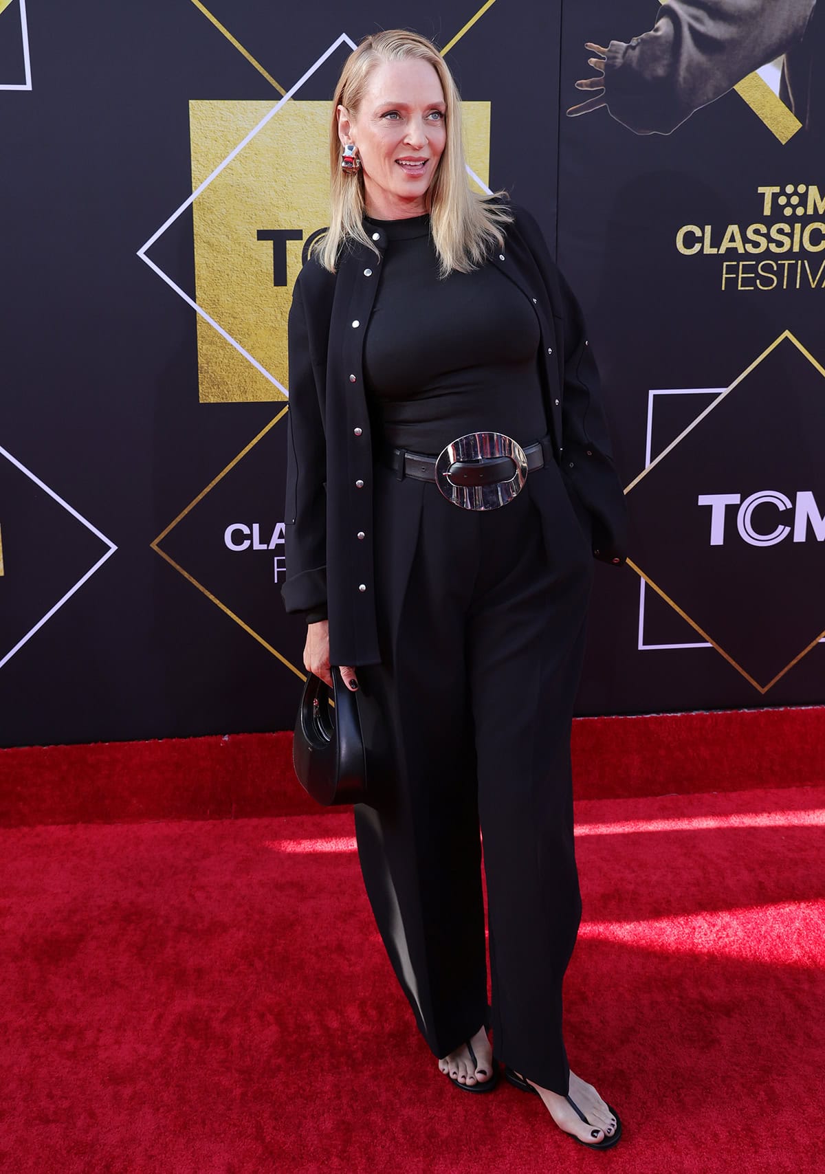 Uma Thurman, who plays Mia Wallace in Pulp Fiction, opts for an all-black ensemble featuring a form-fitting top, straight-leg trousers, and a black jacket