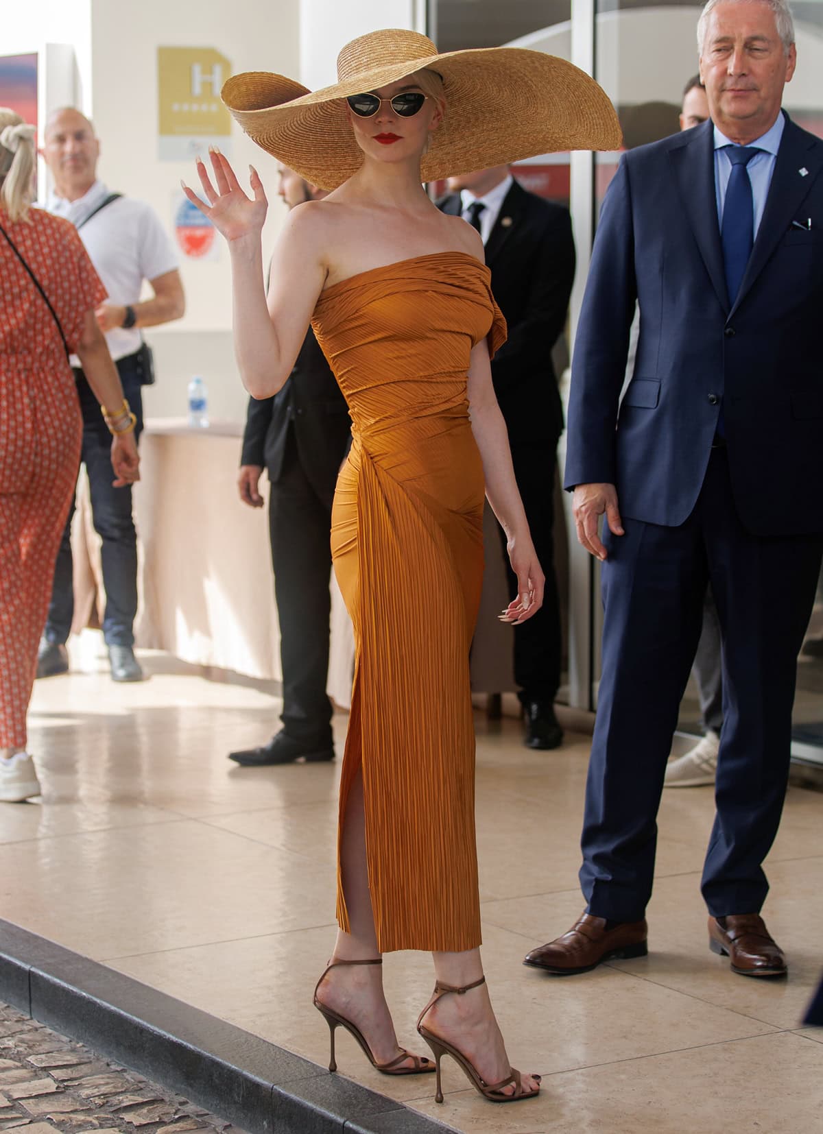 Anya Taylor-Joy made a chic arrival at Hotel Martinez in a vibrant orange Atlein midi-dress paired with Jimmy Choo sandals and an oversized Jacquemus straw hat