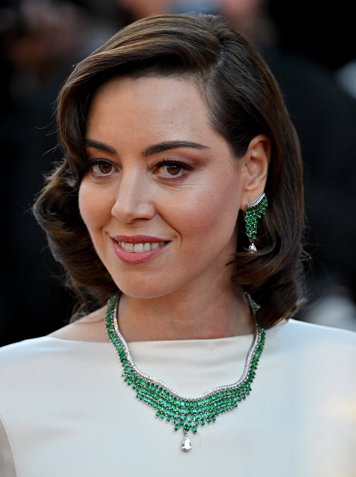 Aubrey Plaza adds color to her white Loewe gown with Piaget Golden Oasis Luxuriant necklace and earrings dripping with emeralds and diamonds