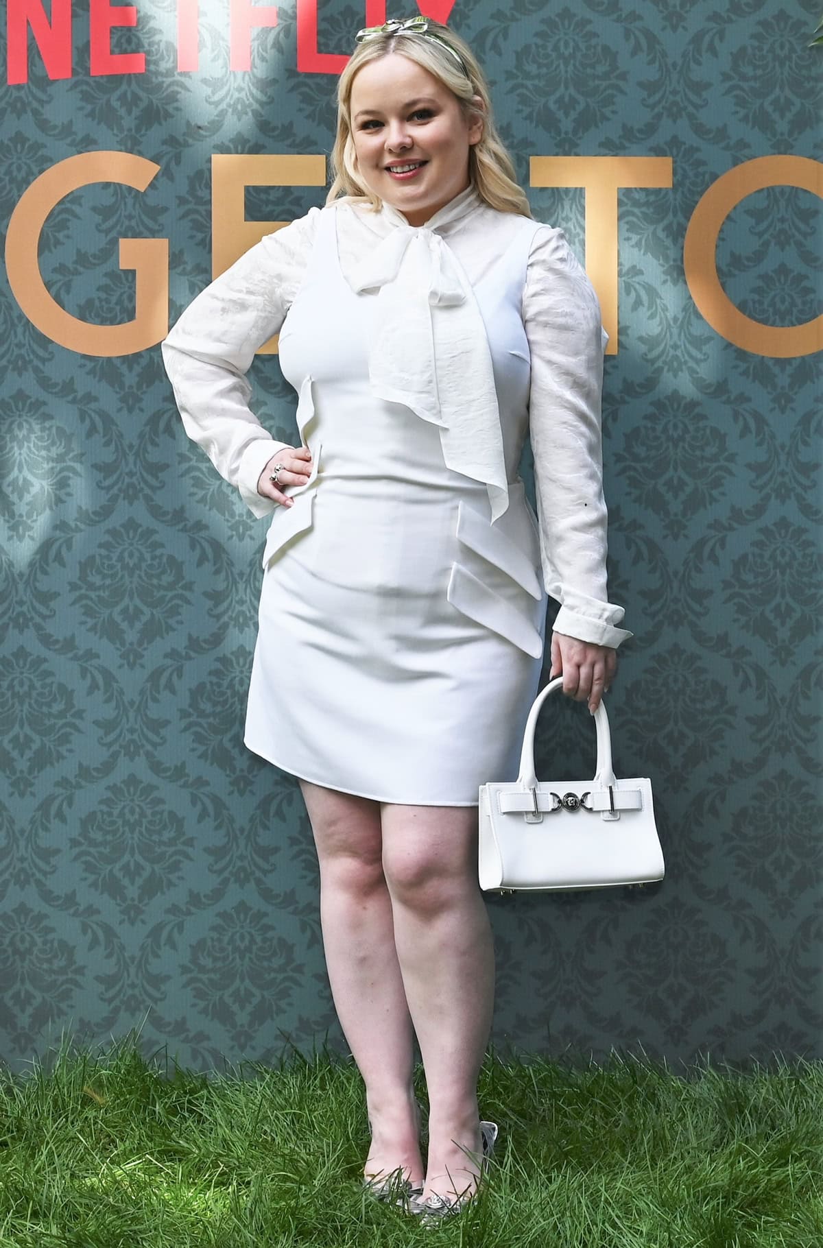 Nicola Coughlan channels the '60s with a sophisticated all-white Versace ensemble, featuring a wool-blend shift mini-dress and sleek accessories at the Bridgerton Season 3 photocall in Milan