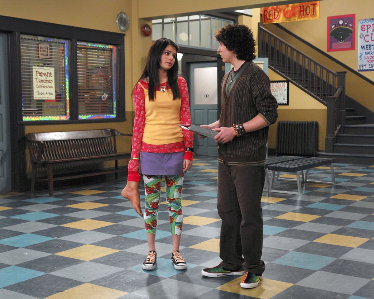 Selena Gomez, as Alex Russo, pairs her playful layered outfit with classic black-and-white Converse Chuck Taylors while chatting with guest star Daryl Sabara in an Episode 1x5 publicity still from Wizards of Waverly Place (2008)