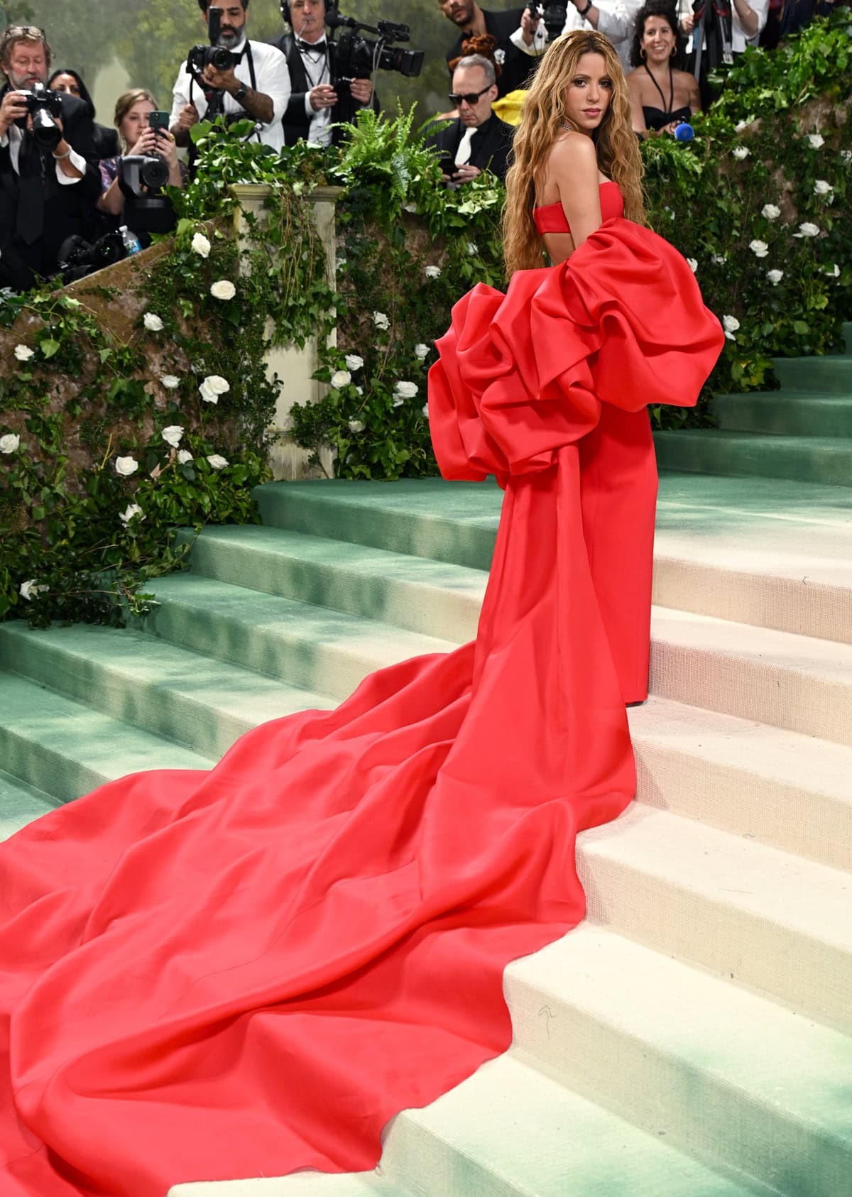 Elegance on the Steps: Captured in the moment, Shakira ascends the Met Gala stairs, her crimson gown trailing gracefully behind her