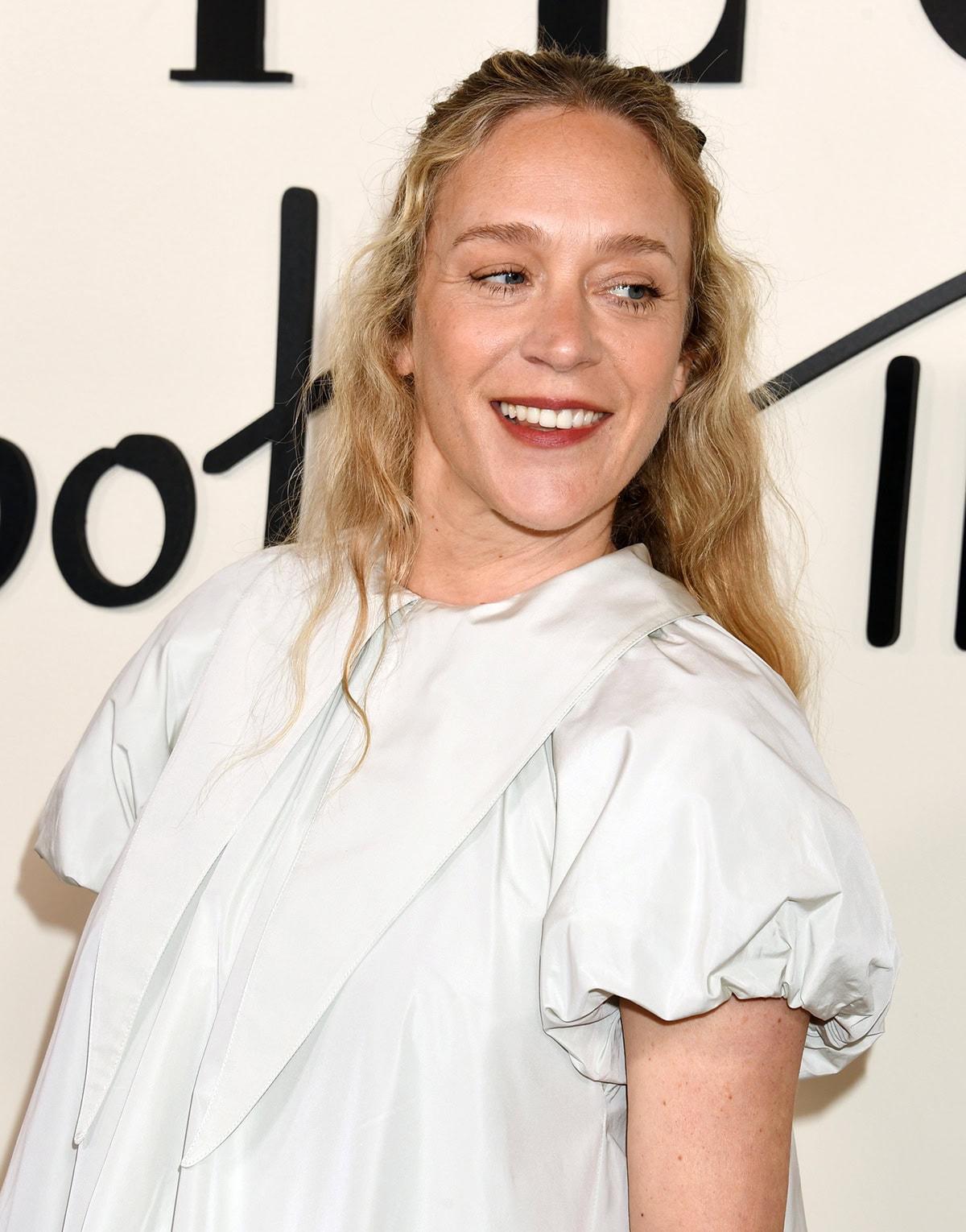 Chloë Sevigny adds a coquette element to her whimsical look by styling her long curly tresses with a black bow