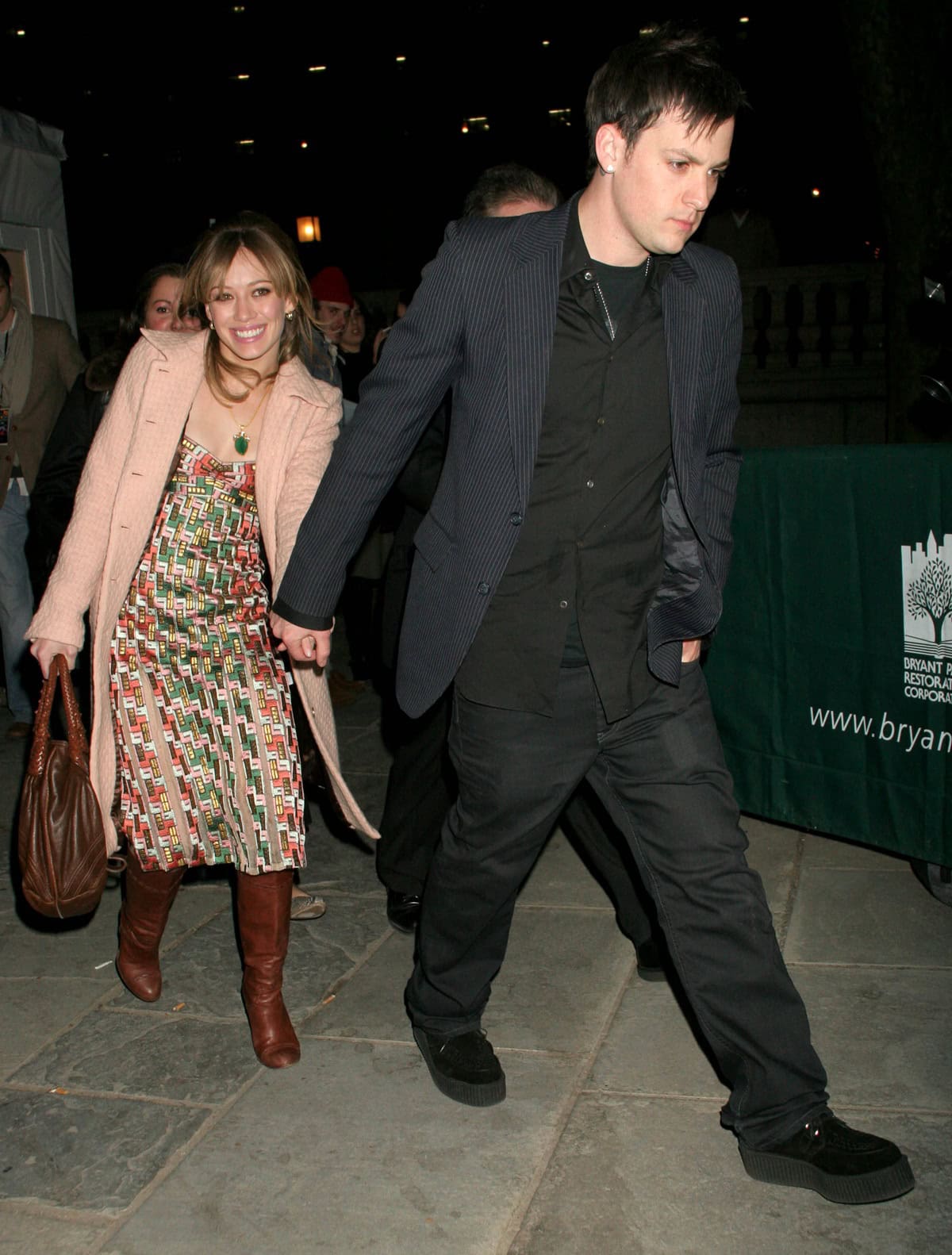On February 9, 2006, Hilary Duff stepped out at Olympus Fashion Week in New York City wearing a printed Zac Posen dress, brown leather boots, a blush pink coat, and carrying a brown Fendi Spy bag, while Joel Madden kept it casual in black with a pinstriped blazer