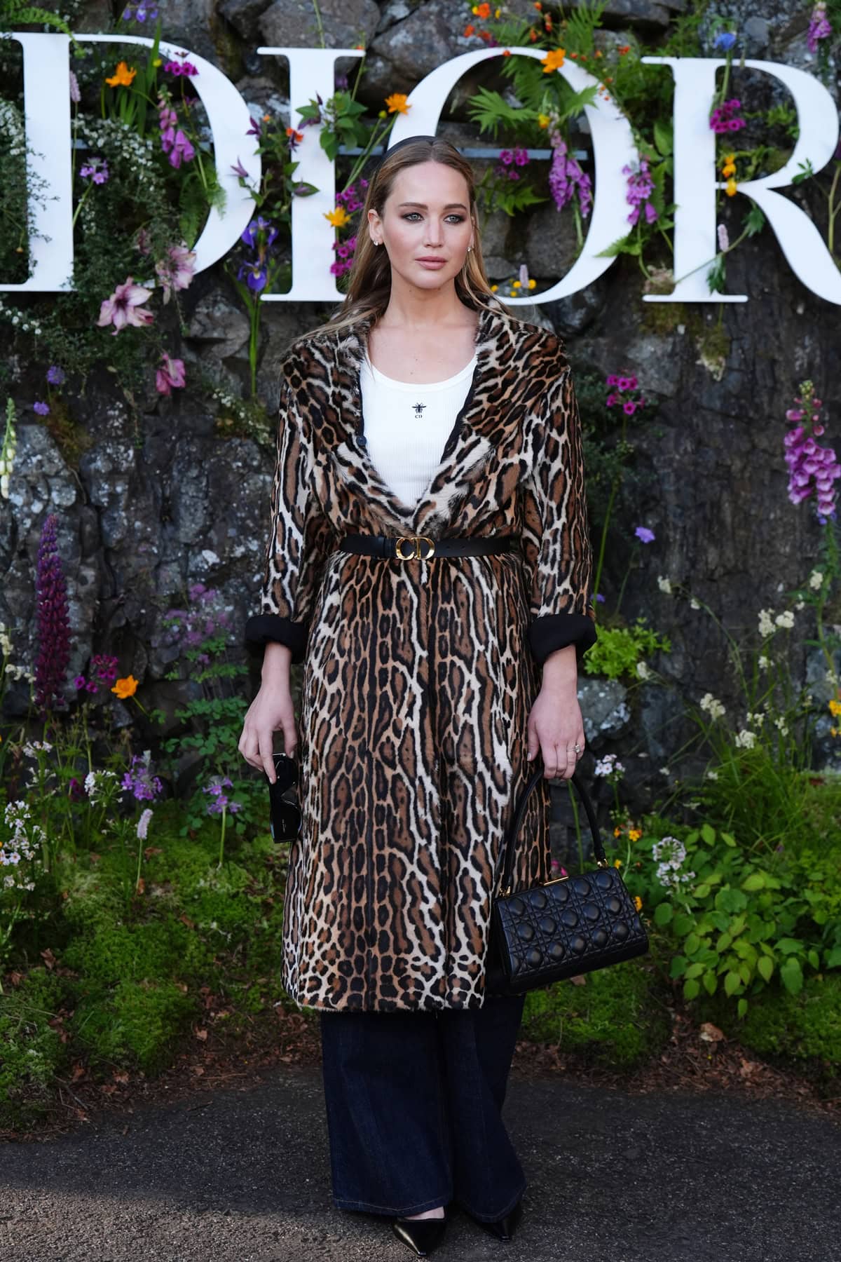 Jennifer Lawrence stunning in a white ribbed Dior tank top and high-waisted denim jeans, embodying understated luxury at Dior's Cruise 2025 collection show