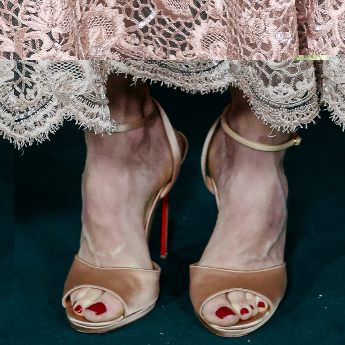 Julie Bowen shows off a glossy red pedicure in nude satin peep-toe ankle-strap heels by Christian Louboutin, revealing the brand’s signature red soles and her elegant, narrow foot shape—likely around a US women’s shoe size 7.5, which she reportedly wears