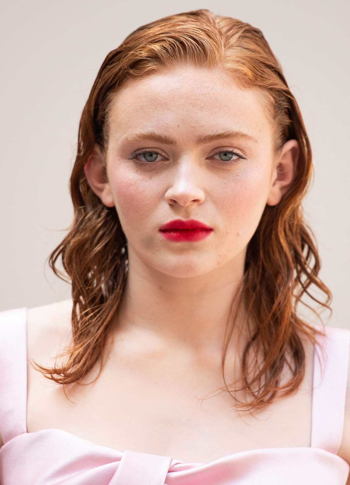 Sadie Sink enhances the outfit's sultry element by styling her ginger tresses in wet-look curls and wearing hot pink lipstick