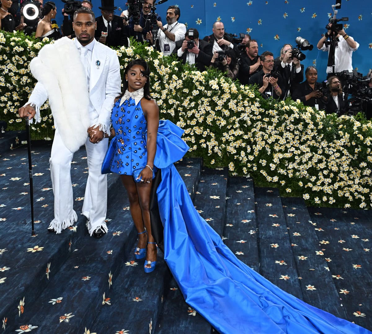 Simone Biles wore a custom Harbison Studio gown and blue Aquazzura platforms, while Jonathan Owens complemented her in a white Deji & Kola suit with Christian Louboutin shoes and accessories by Margot McKinney, Audemars Piguet, and Daniel’s Leather at the 2025 Met Gala
