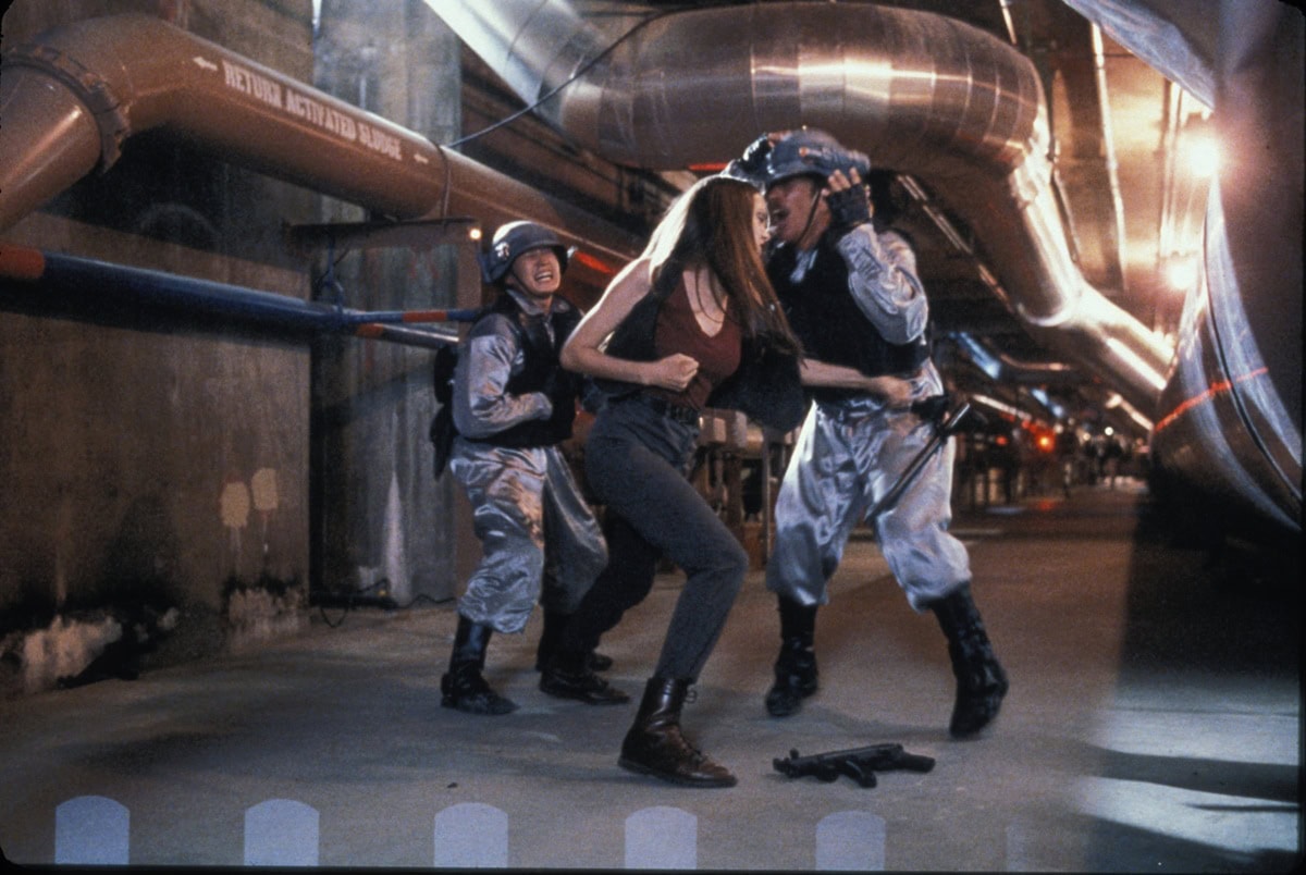 Angelina Jolie battles guards in Cyborg 2 wearing combat boots, tapered high-waisted pants, and a sleeveless top—an early glimpse of her tough, action-ready style