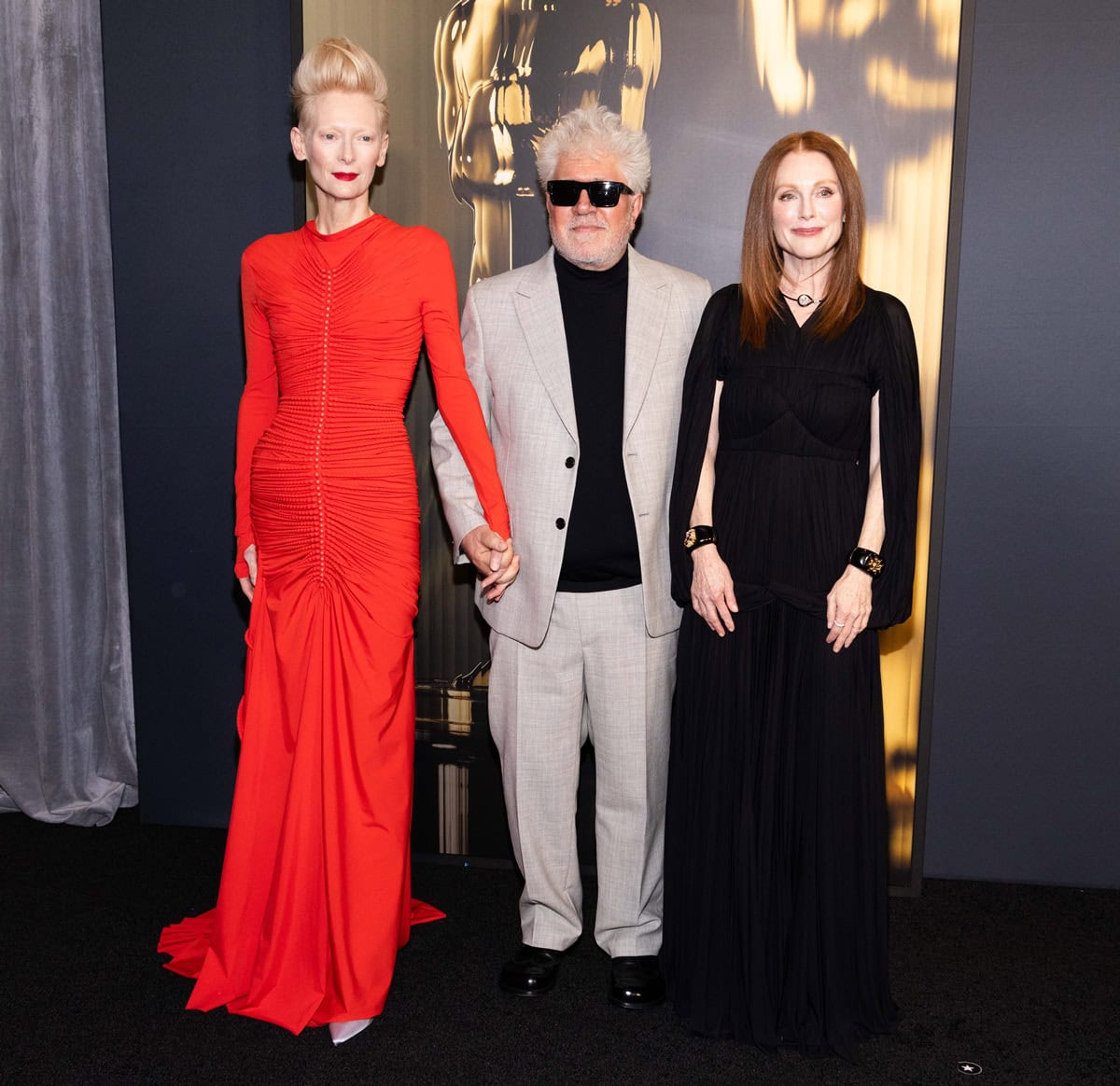Julianne Moore appears petite beside Tilda Swinton and Pedro Almodóvar at the 15th Governors Awards, wearing a flowing black Proenza Schouler “Rumi” dress styled with bold Verdura cuffs and a Belperron necklace