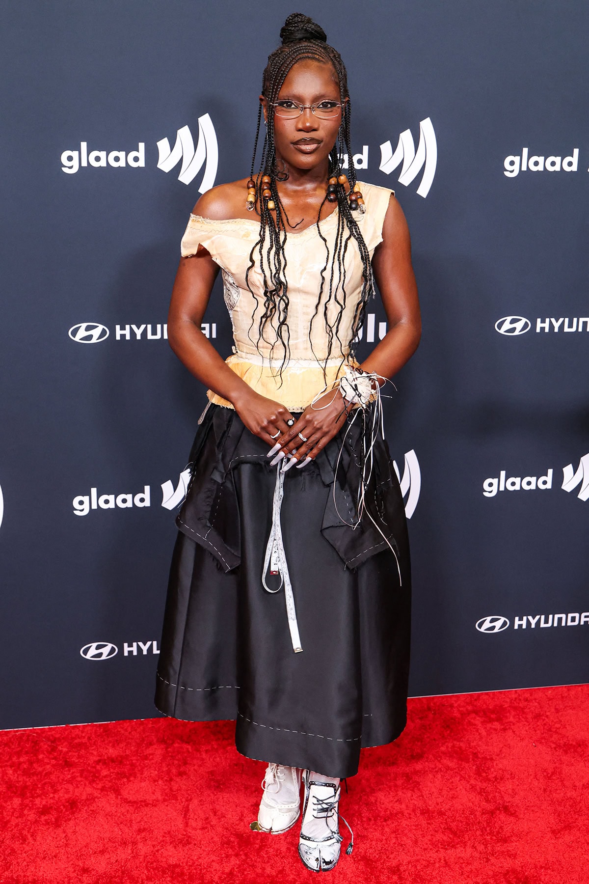 Doechii teams her brogue x pump hybrid shoes with a deconstructed outfit from Maison Margiela featuring an apricot viscose and taffeta decortiqué corset top and a black A-line midi skirt with exposed seams and loose fabric around the waist