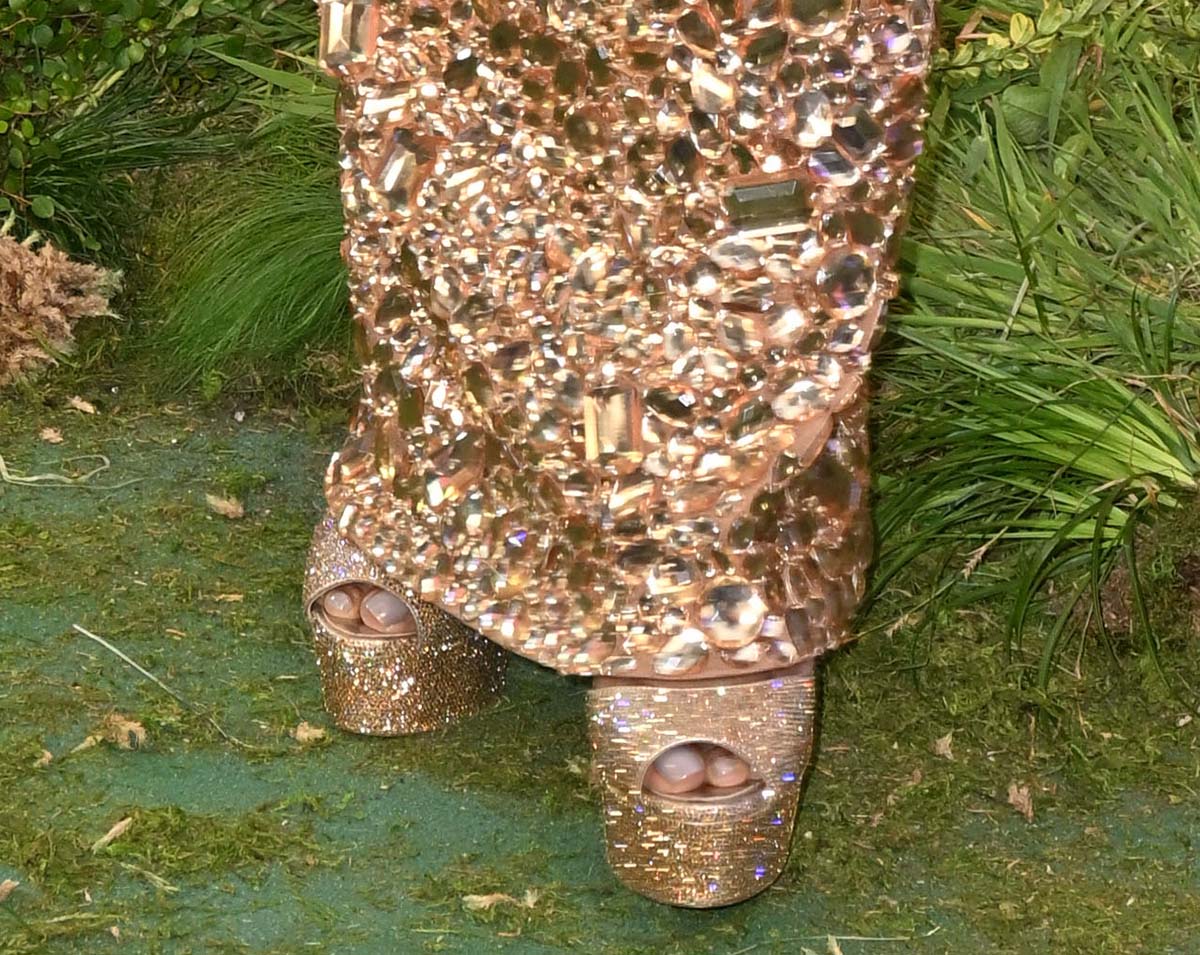 Angela Bassett elevates her look with crystal-embellished gold platform pumps featuring chunky heels and peep toes that showcase her nude pedicure while adding serious height and sparkle