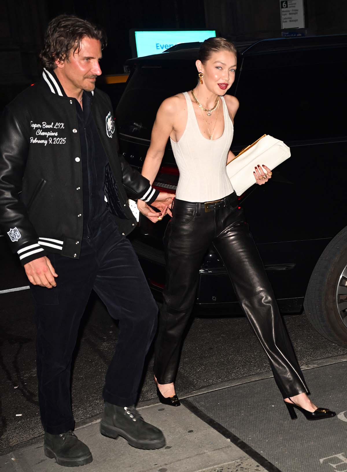 Gigi Hadid walks hand-in-hand with Bradley Cooper in a white Schiaparelli wool jersey corset bodysuit and black leather pants by Khaite