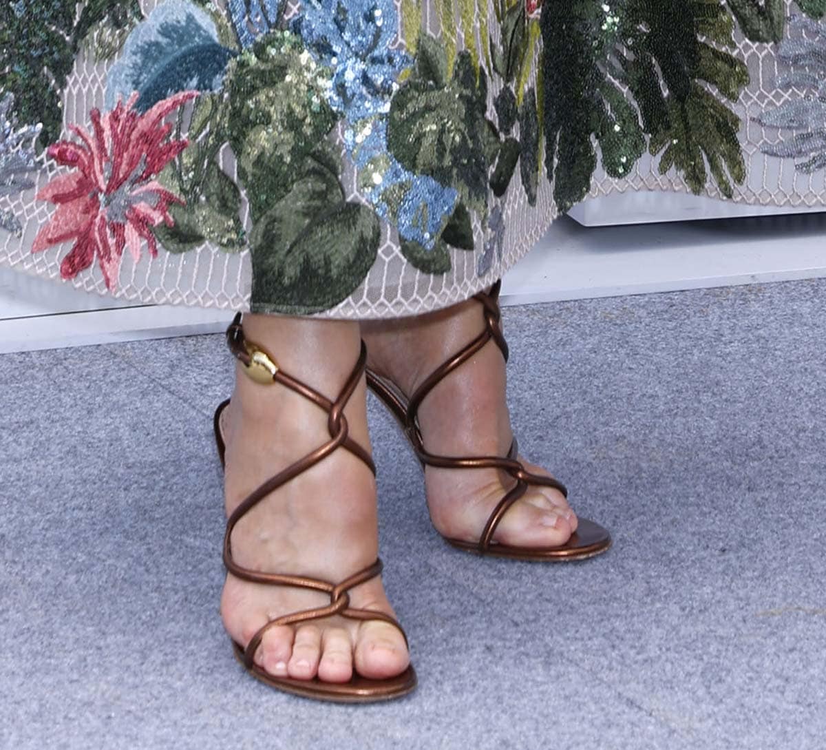 Hannah Waddingham pairs her floral embroidered dress with strappy bronze sandals featuring sculptural curved straps and gold buckle accents that add a touch of vintage glam