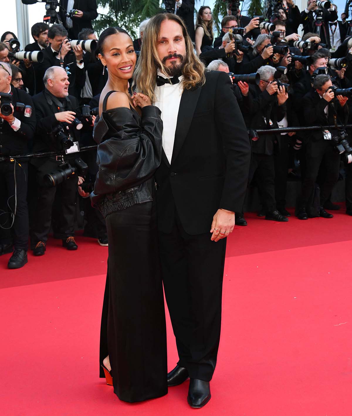 Zoe Saldana elevates her Saint Laurent LBD with statement wedge sandals, while husband Marco Perego complements her sleek look in classic black dress shoes and a sharp tuxedo