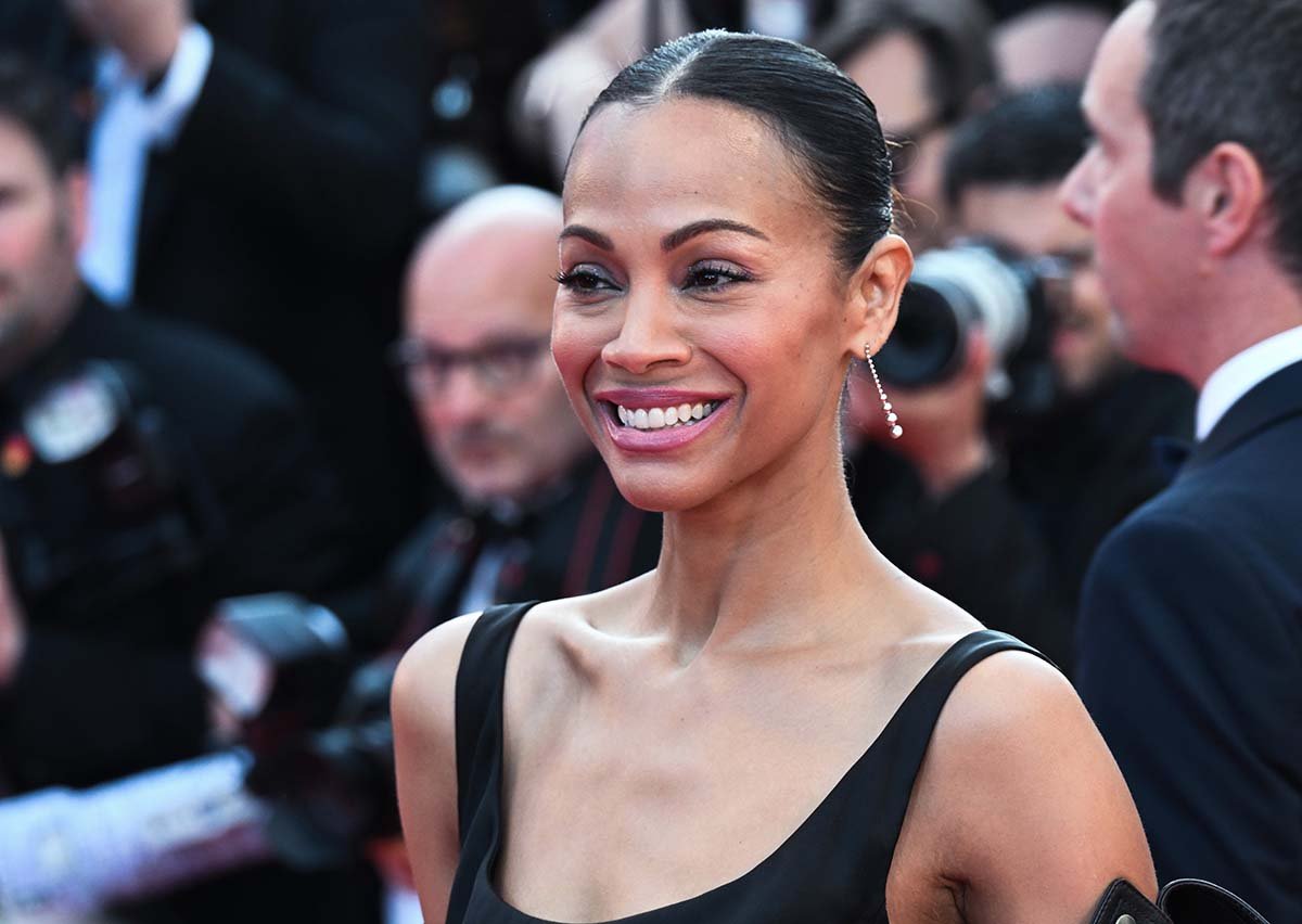 Zoe Saldana styles her hair in a slick center-parted bun and wears minimal makeup with pink lipstick and mascara
