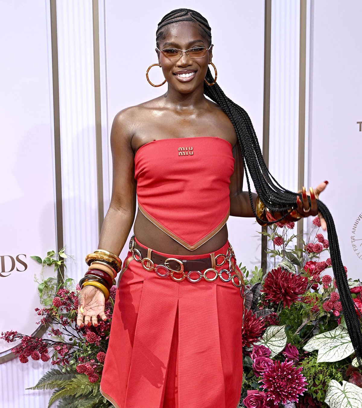 Doechii pairs her cute Jimmy Choo Flower sandals with a Y2K-style bright red ensemble from Miu Miu, composed of a strapless bandana crop top and a pleated knee-length skirt