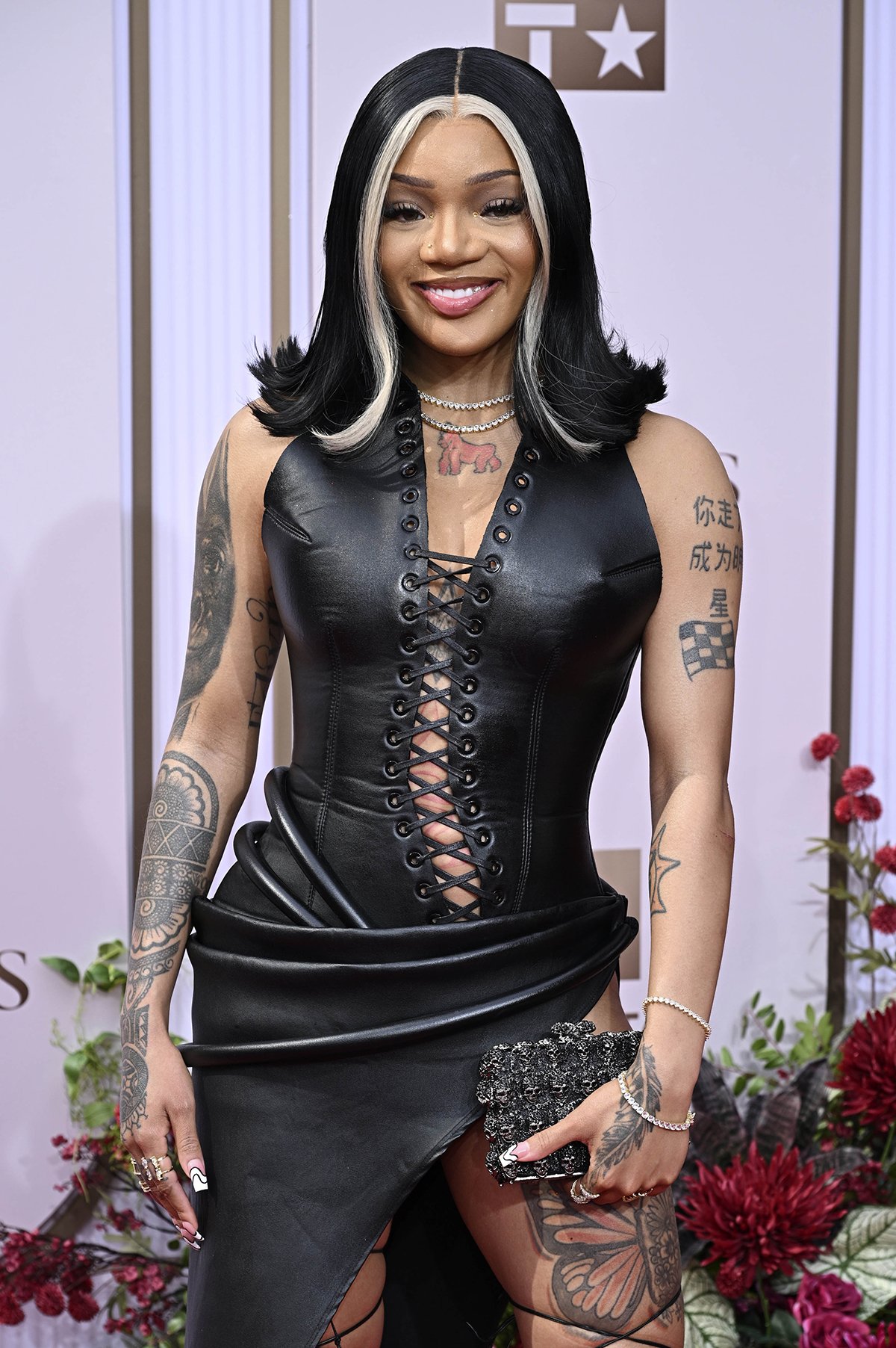 GloRilla showcases her risque fashion sense by wearing a black leather corset dress with a draped waist and a daring asymmetrical skirt
