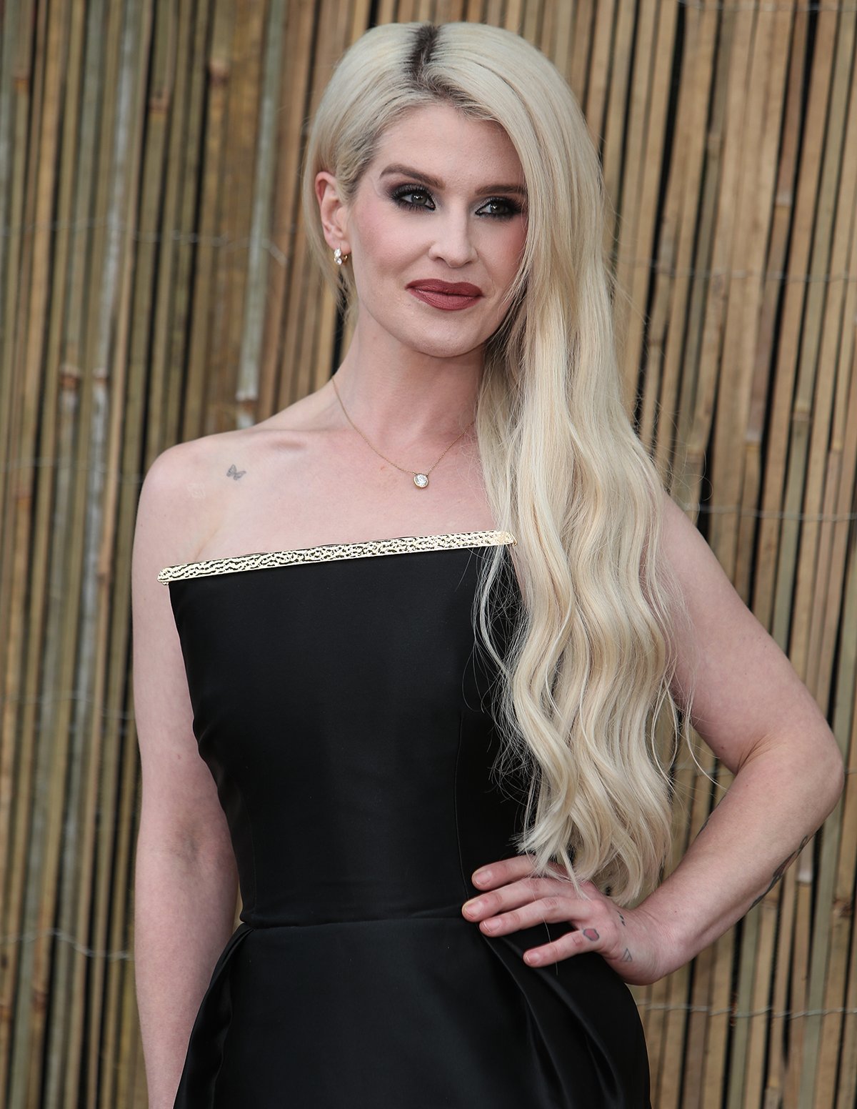 Kelly Osbourne pairs her strappy black platform sandals with a minimalist black Rebecca Vallance dress featuring a gold-trimmed neckline