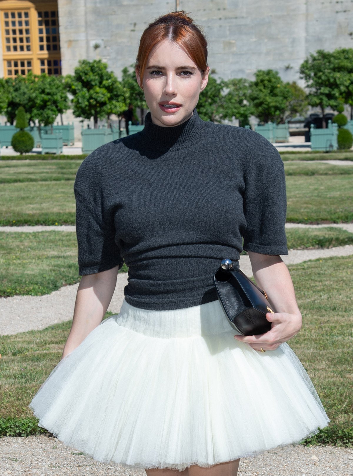 Emma Roberts keeps her ensemble minimalist, accessorizing with just a black Jacquemus La Pochette Rond Carré leather clutch and her engagement ring