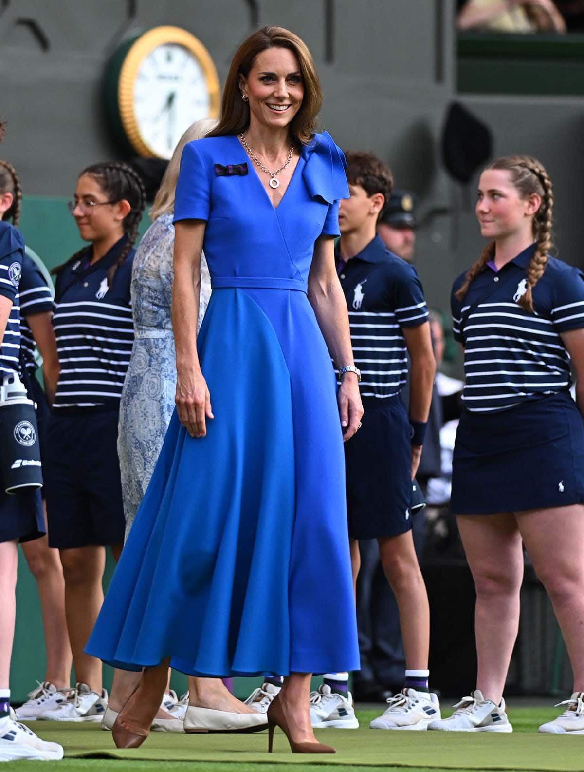 Catherine, Princess of Wales, exudes classic summer elegance in a blue Roksanda V-neck dress with a bow on one shoulder, a waistband, and a color-blocked midi skirt