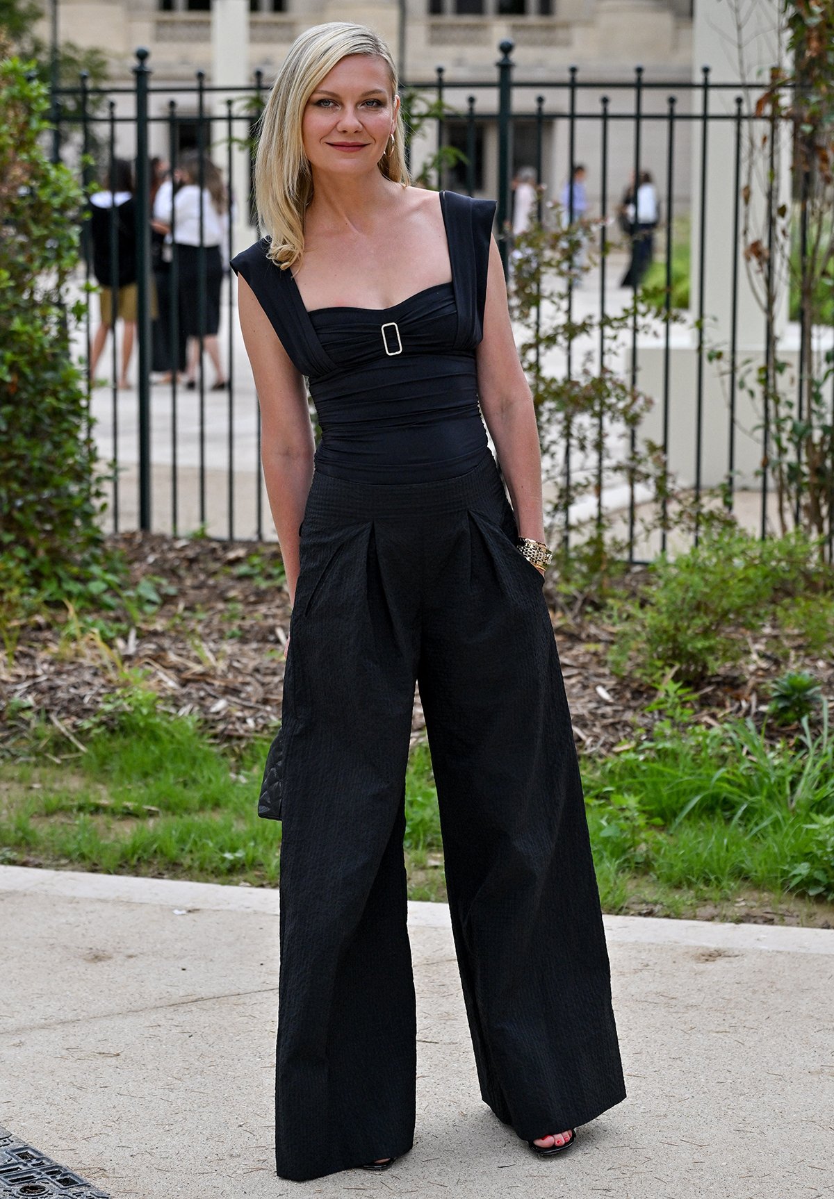 Kirsten Dunst exudes effortless Parisian chic in a black ruched bodysuit with wide shoulder straps and a decorative buckle and wide-leg trousers cut from seersucker-like fabric
