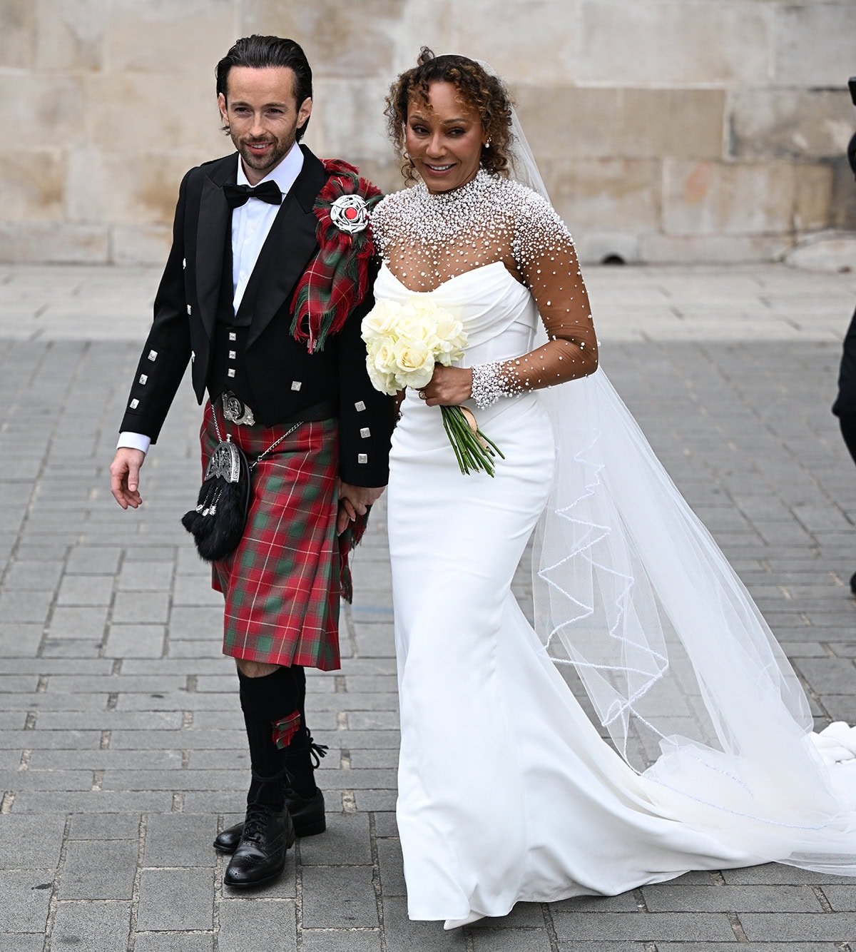Mel B looks stunning in a white wedding dress designed by Josephine Scott with a structured pleated bodice, a plunging neckline, and a sheer panel with multi-sized pearl embellishments
