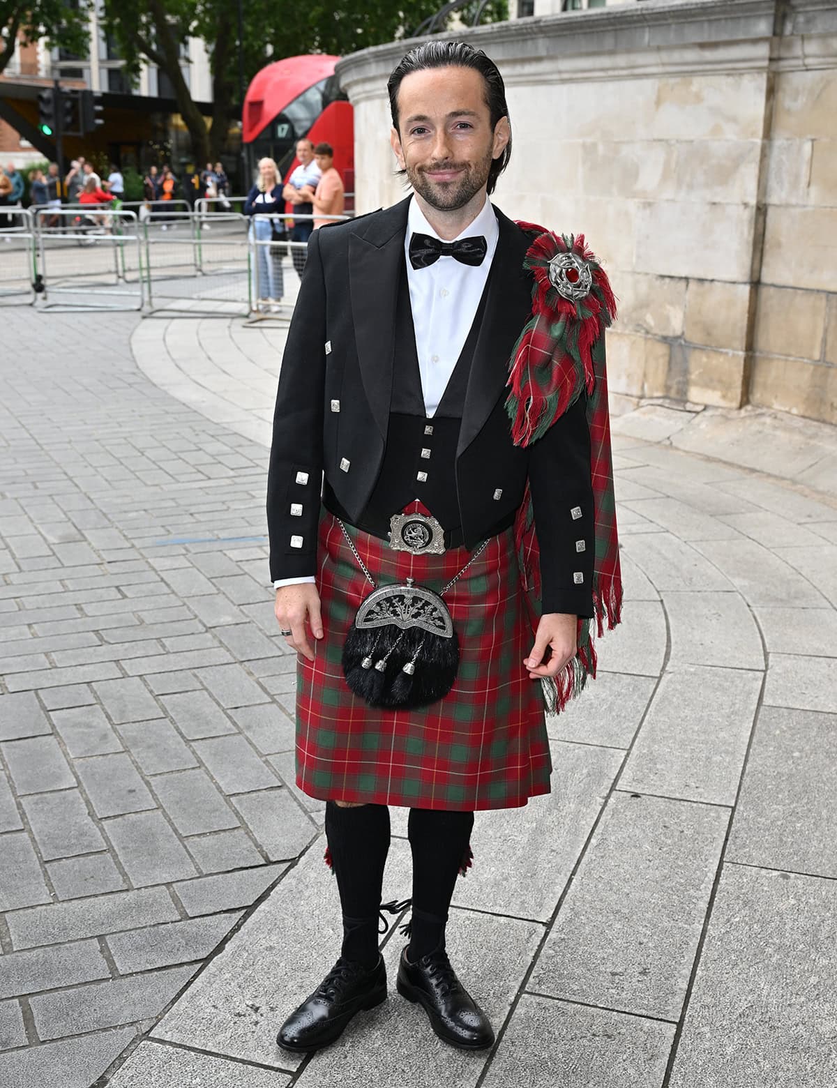 Rory McPhee embraces tradition in a Scottish formal outfit, featuring a Prince Charlie jacket, a green and red plaid kilt with a matching fly plaid, a sporran, and a pair of ghillie brogues