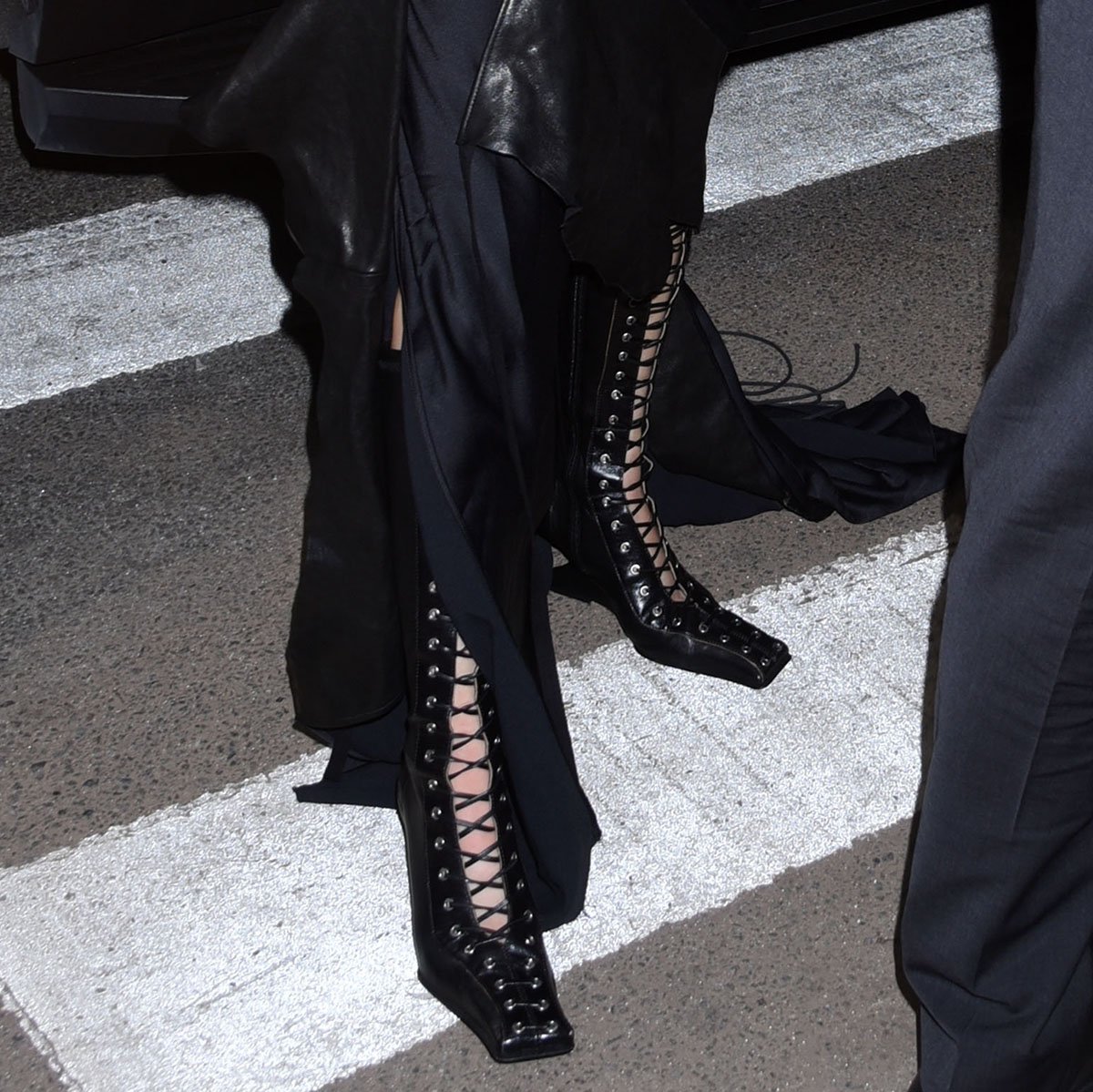 Jenna Ortega teams her deconstructed slip dress with black leather lace-up boots by Miista featuring silver eyelets, square toes, black leather laces, and angular wedge heels