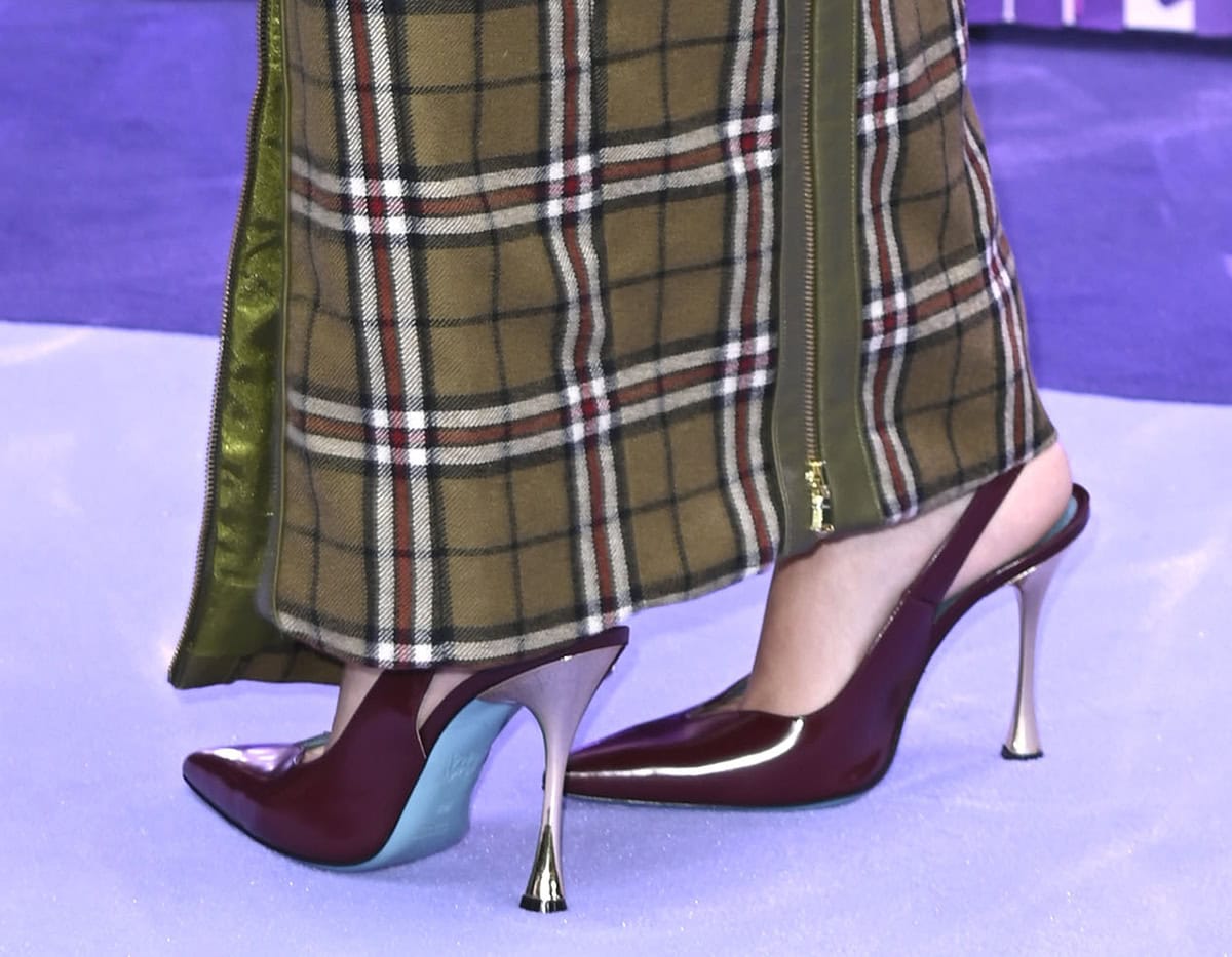 Julia Butters gives her olive green ensemble a pop of unexpected color with burgundy Valentina Rangoni Single slingback pumps featuring sweetheart vamps, flared metal heels, and teal soles