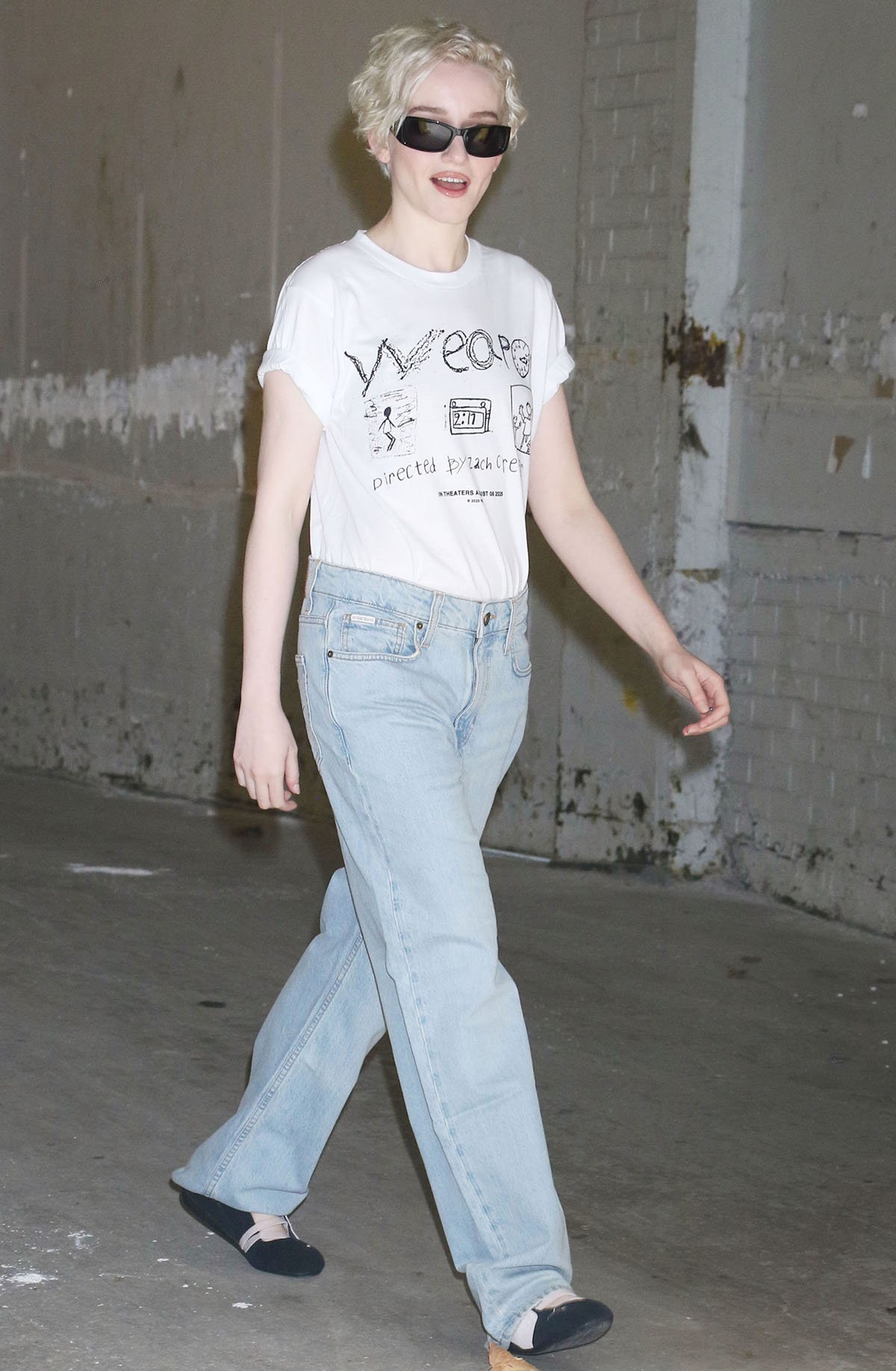 Julia Garner visits Watch What Happens Live with Andy Cohen in Guess jeans and a white graphic tee featuring a hand-drawn-style graphic advertising Weapons