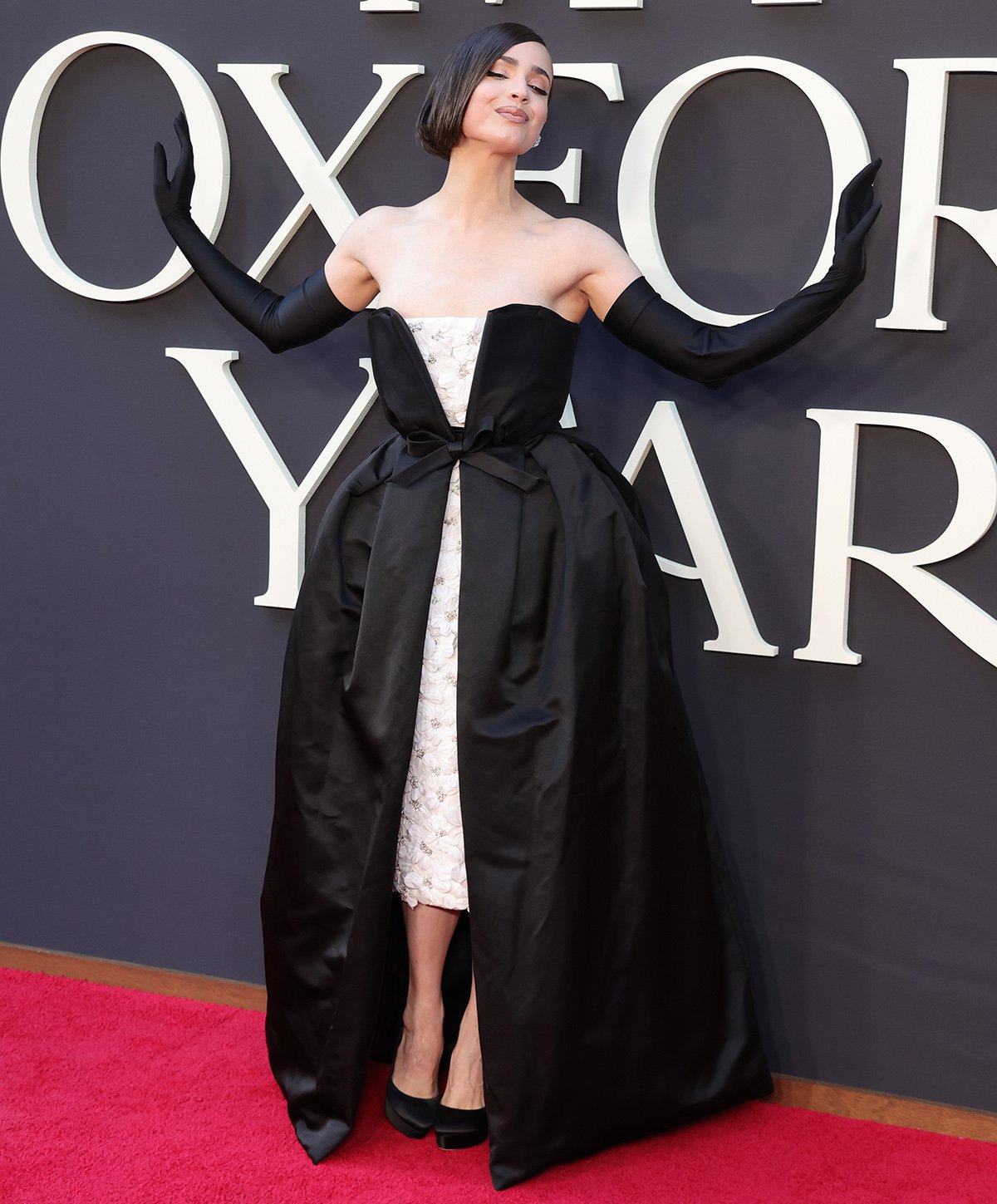 Sofia Carson embraces modern romance in a black and white layered gown by Richard Quinn featuring a white strapless midi dress embroidered with 3D flowers and a detachable black satin gown with a bow at the waist at the LA premiere of My Oxford Year